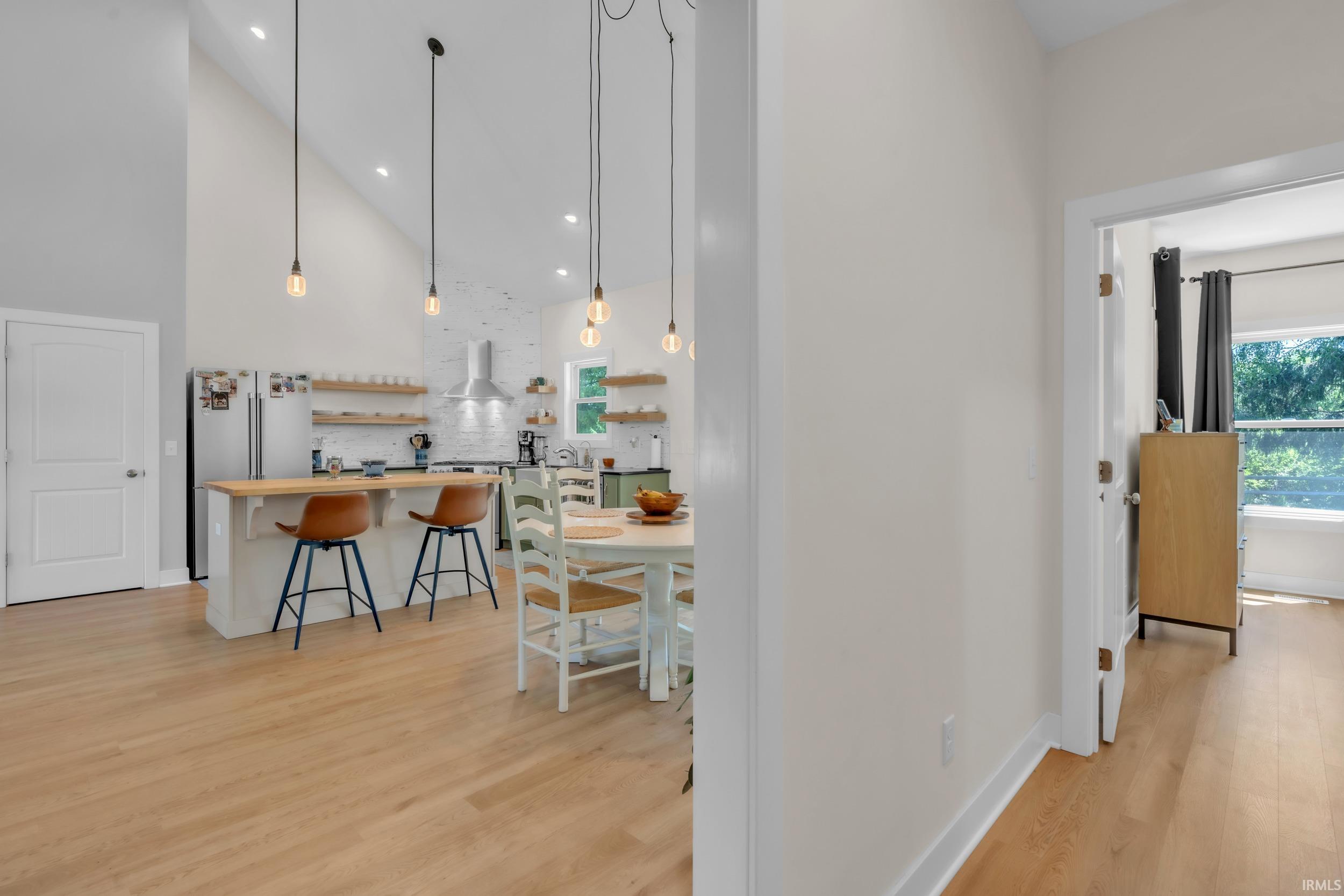 Vaulted ceiling kitchen featuring a central island with wood countertop, stainless steel appliances, open shelving, and pendant lighting