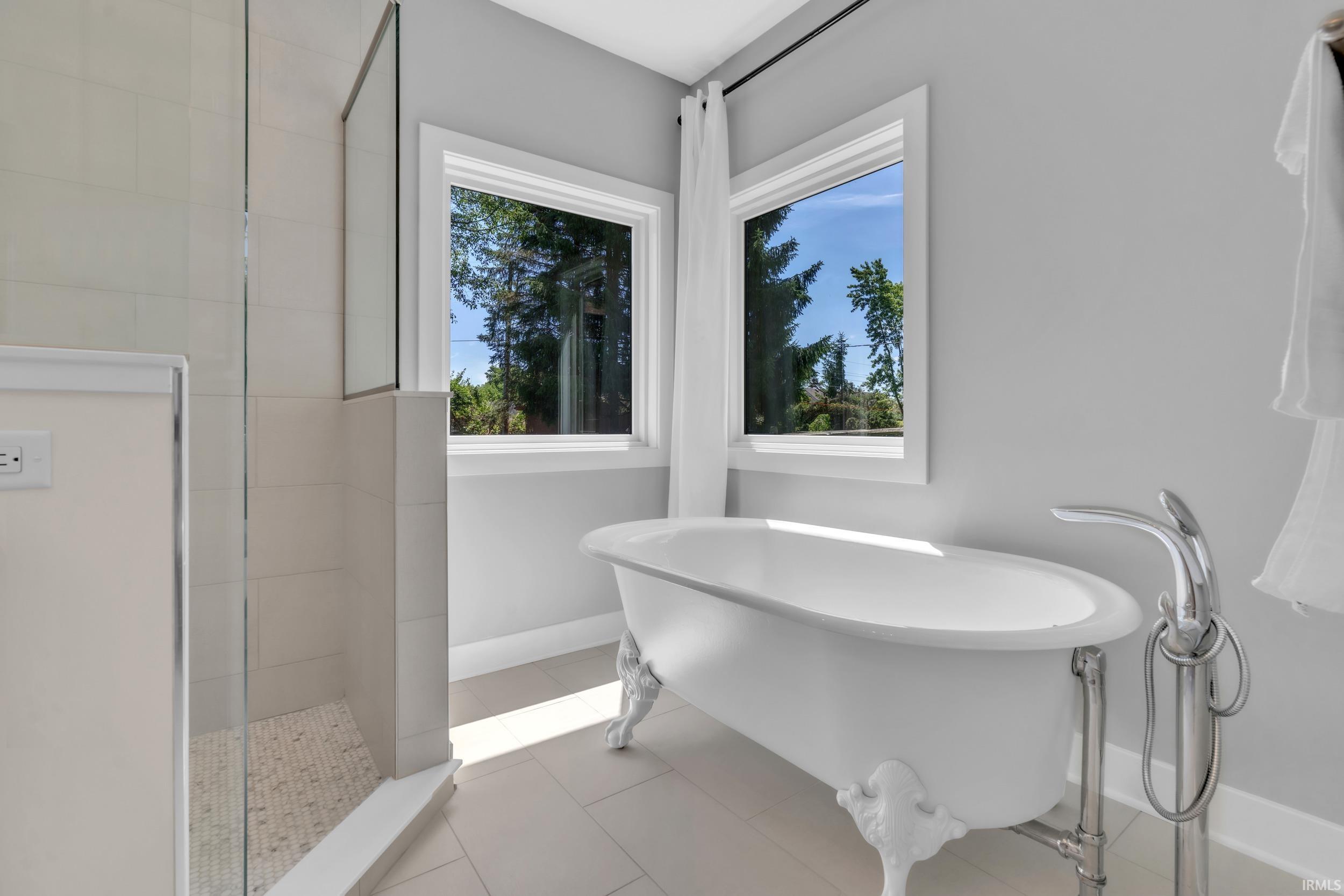 Freestanding clawfoot tub with floor-mounted chrome faucet, set against two bright windows