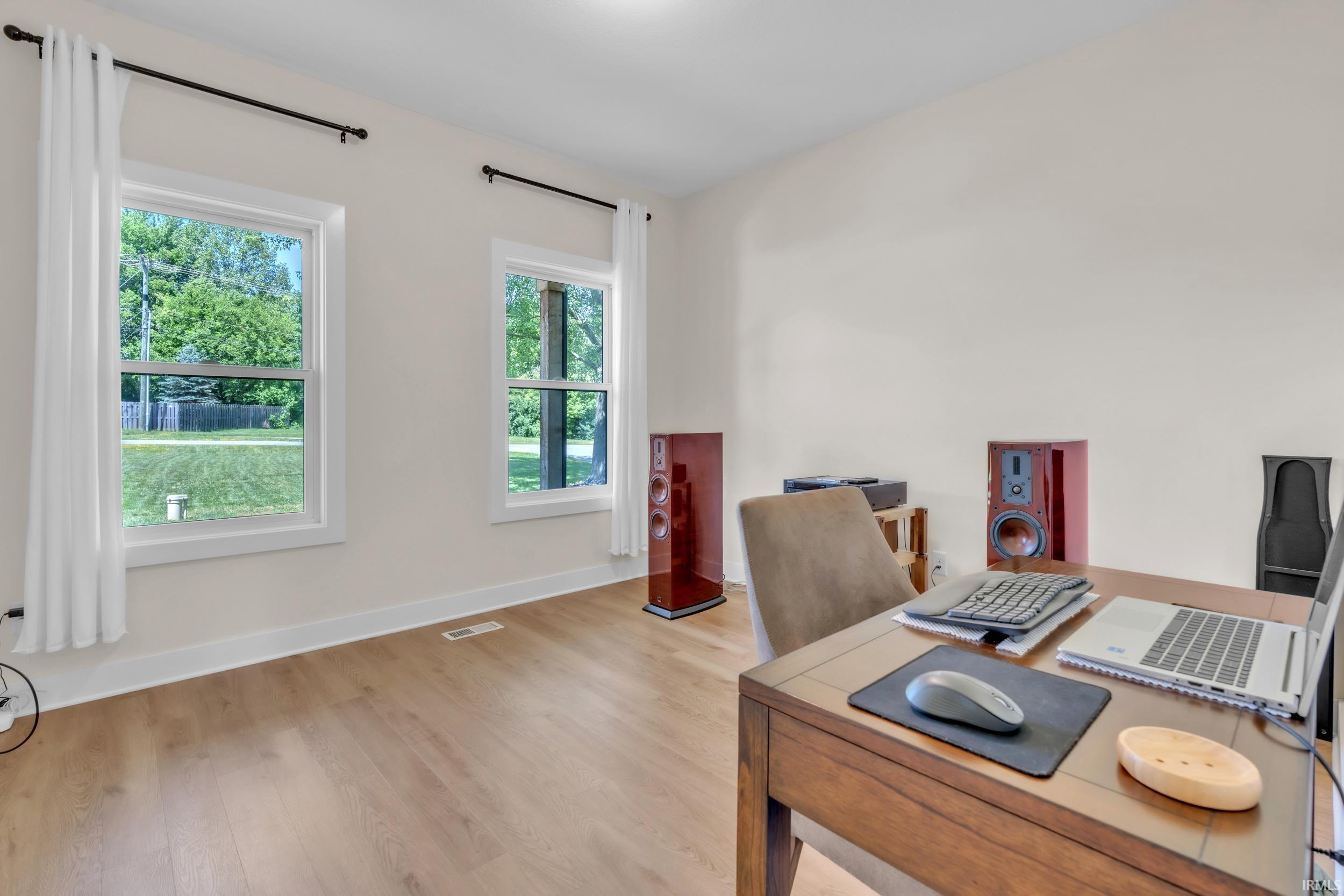 Room featuring light-toned walls, wood-finish flooring, white window trim, and white baseboards