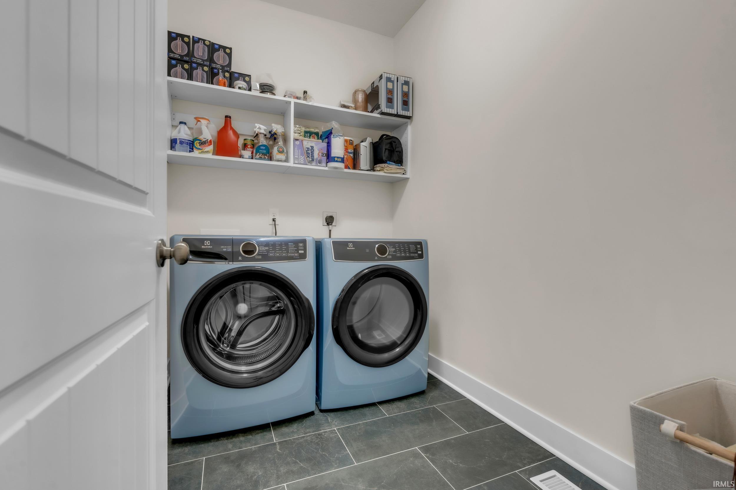 Dedicated laundry area featuring a washer and dryer, dark tile flooring, and integrated wall shelving