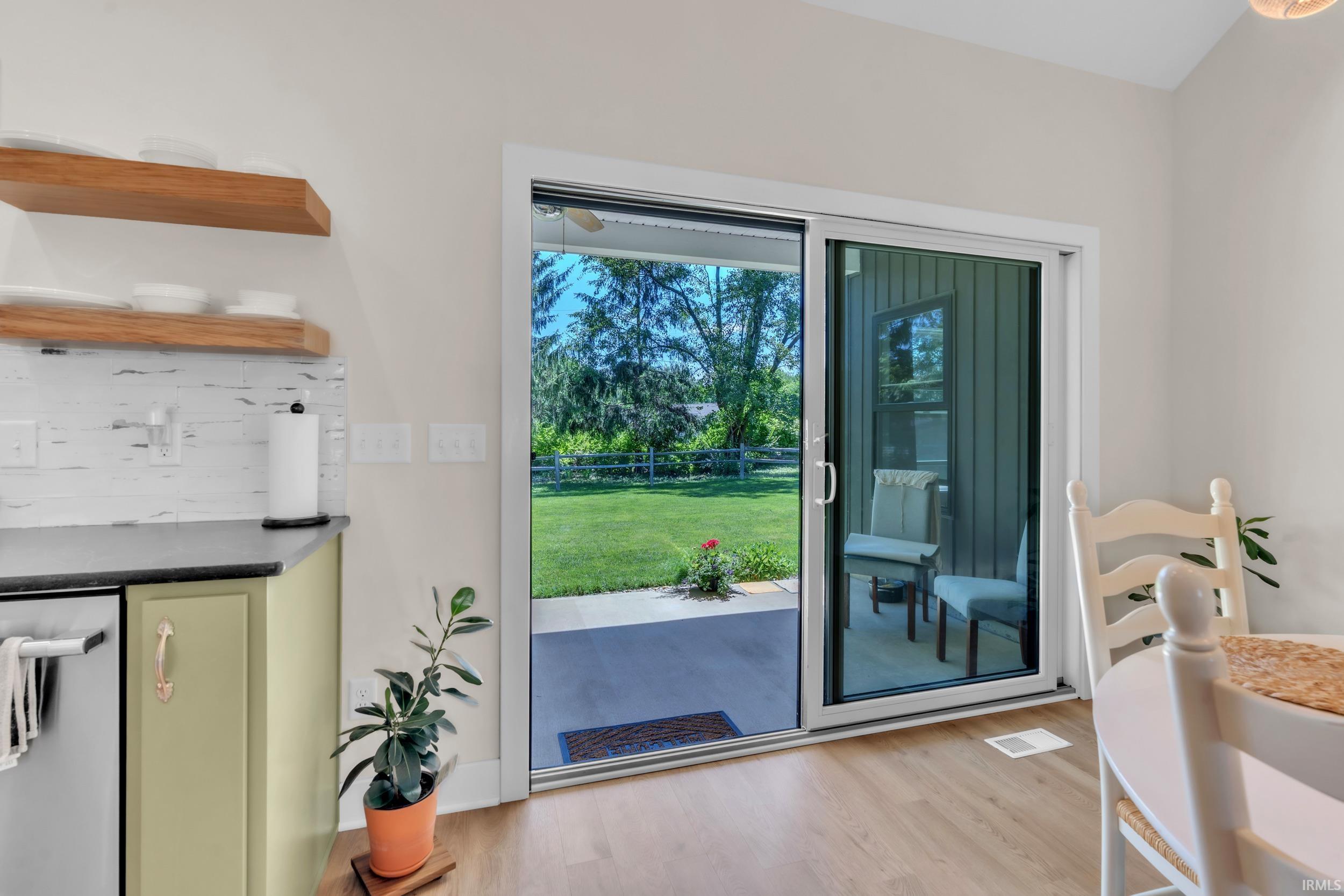 Sliding glass door opening to an outdoor patio with a concrete surface, bordered by a green lawn and mature trees
