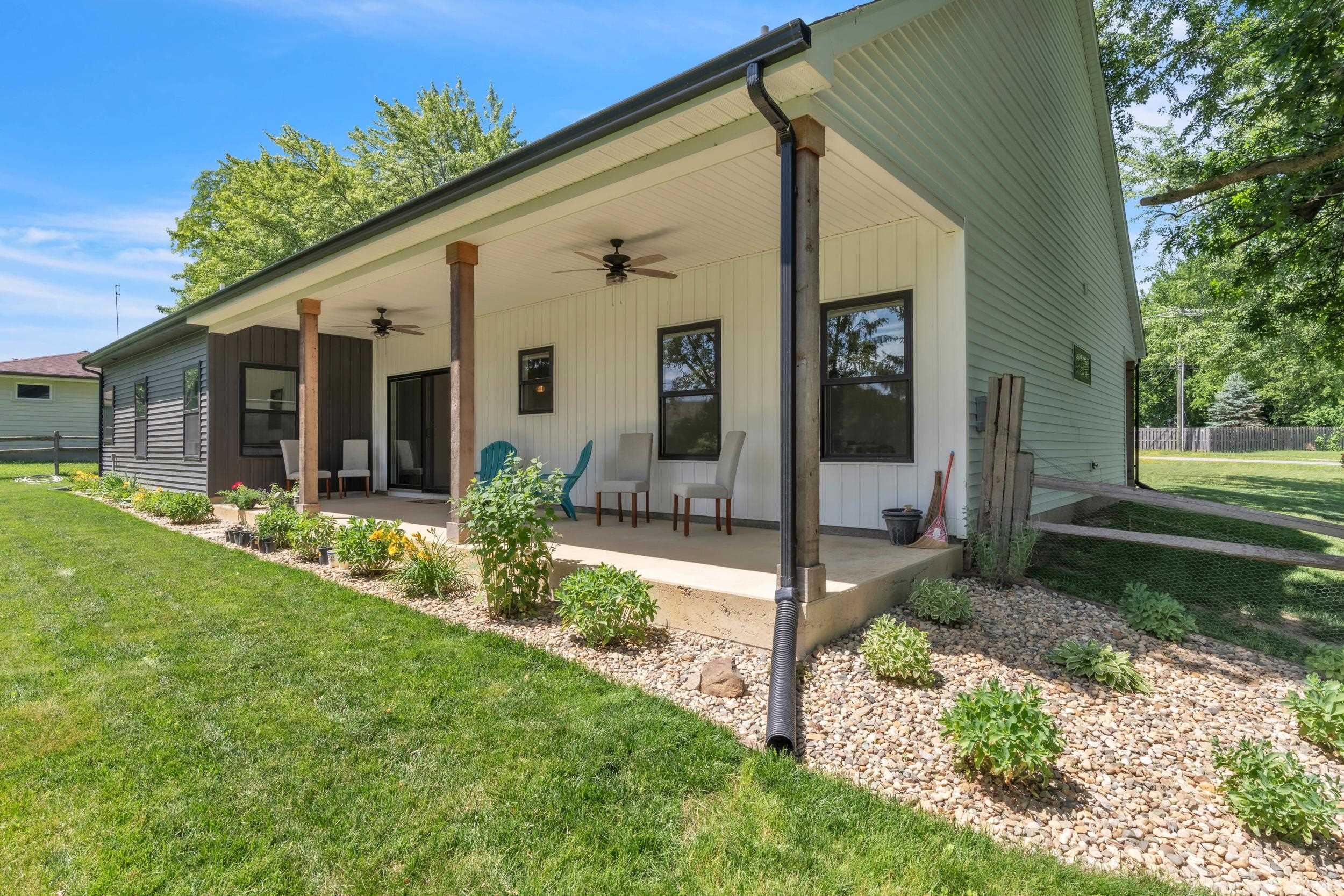 Inviting covered patio with dark-framed windows, white vertical siding, and exposed wood support beams