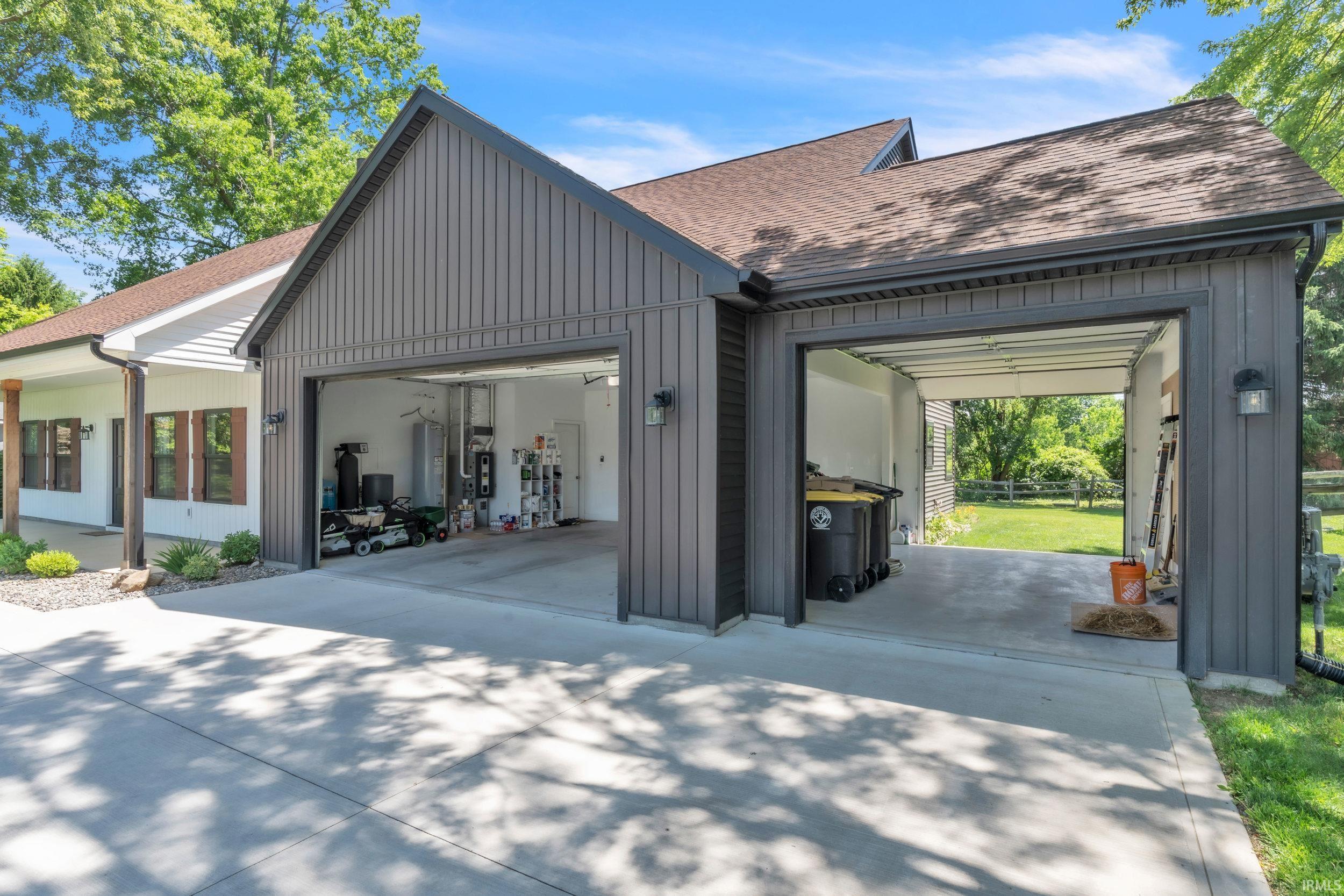Expansive concrete driveway leading to a two-door garage with dark gray vertical panel siding and brown shingle roofing