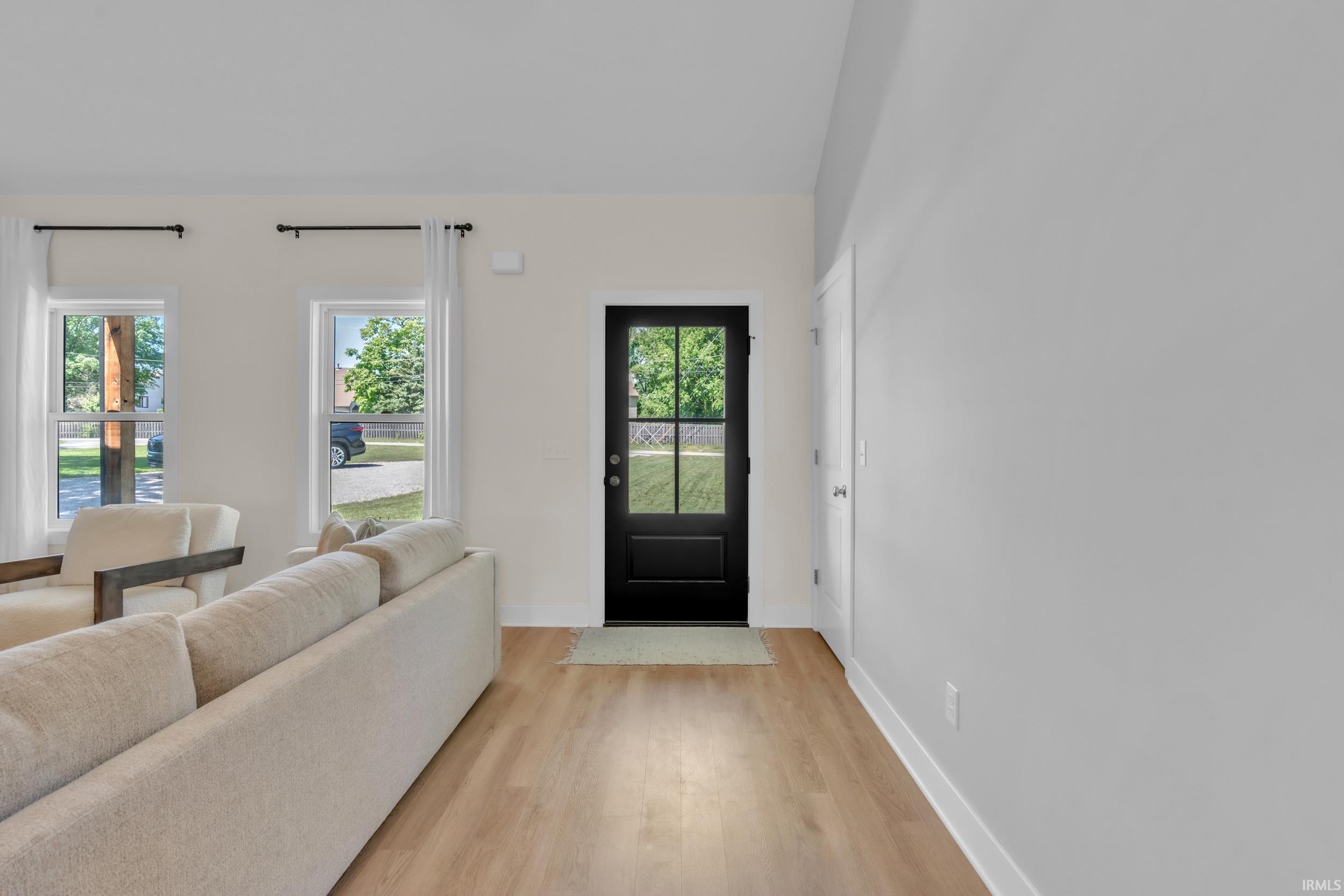 Inviting entryway featuring a dark-paneled door with glass inserts, light wood-finish flooring, and crisp white baseboards