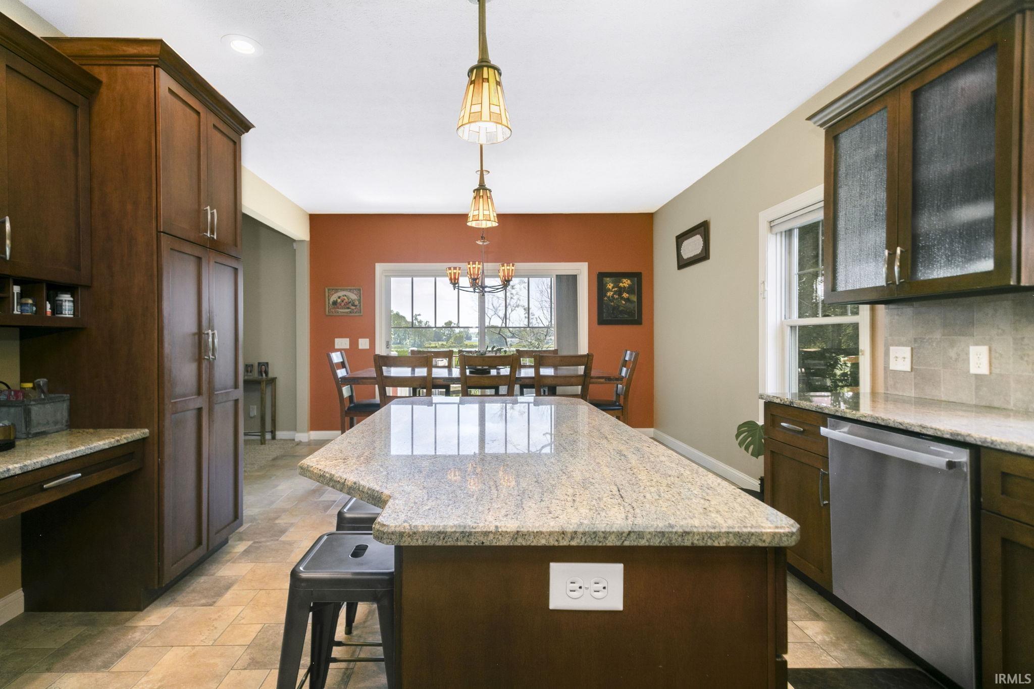 Kitchen featuring a large island with stone countertop, stainless steel dishwasher, tile flooring, and dark wood-finish cabinetry