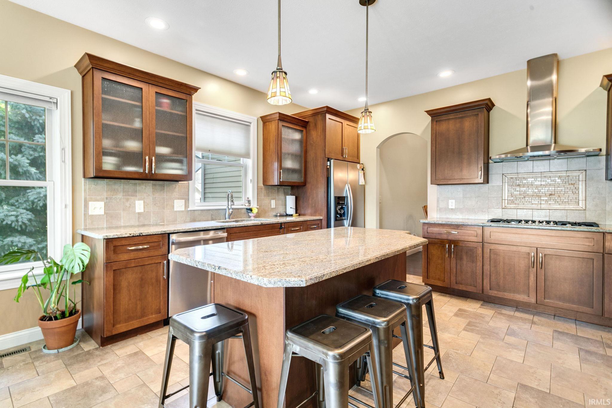 Kitchen featuring recessed lighting, a central island with countertop seating, wood cabinetry with some glass-front uppers, stainless steel appliances, and a tiled backsplash