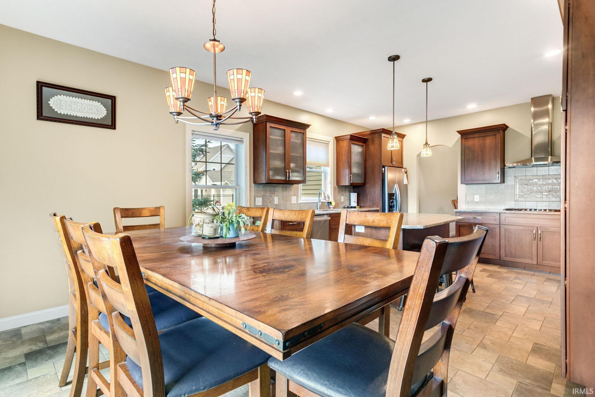 Open-concept kitchen and dining area featuring wood cabinetry, stainless steel appliances, a kitchen island with seating, a decorative tile backsplash, and recessed lighting