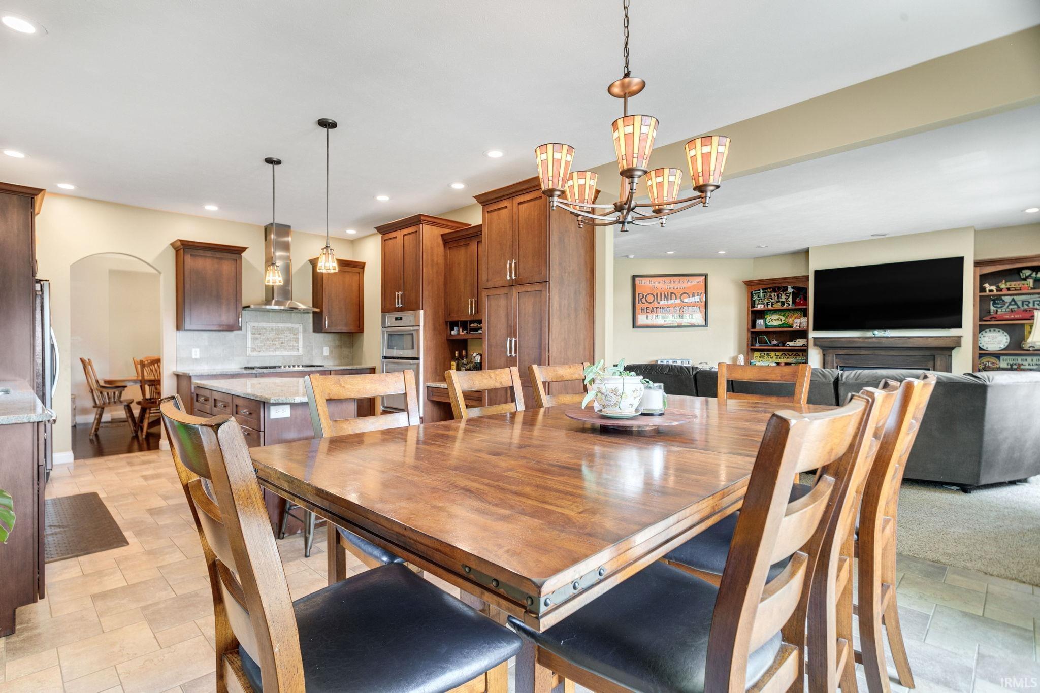 Dining area featuring a wood-finish table with studded trim, an ornate chandelier, tile flooring, and integrated lighting