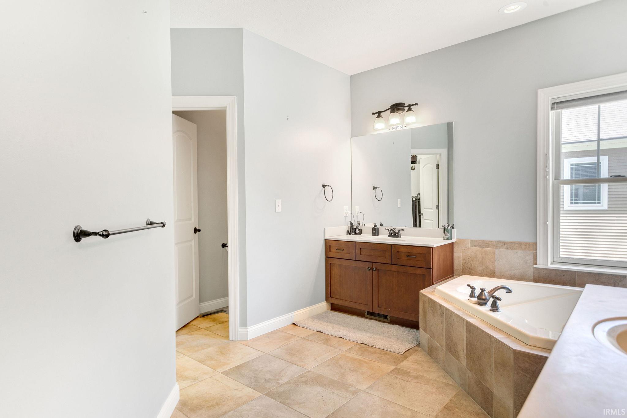 Bathroom featuring a large soaking tub, tile flooring, a double vanity with a mirror, and a window