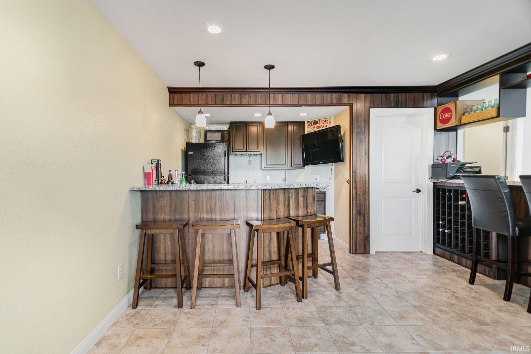 Built-in bar featuring a granite-style countertop, wood-finish paneling, and a black refrigerator