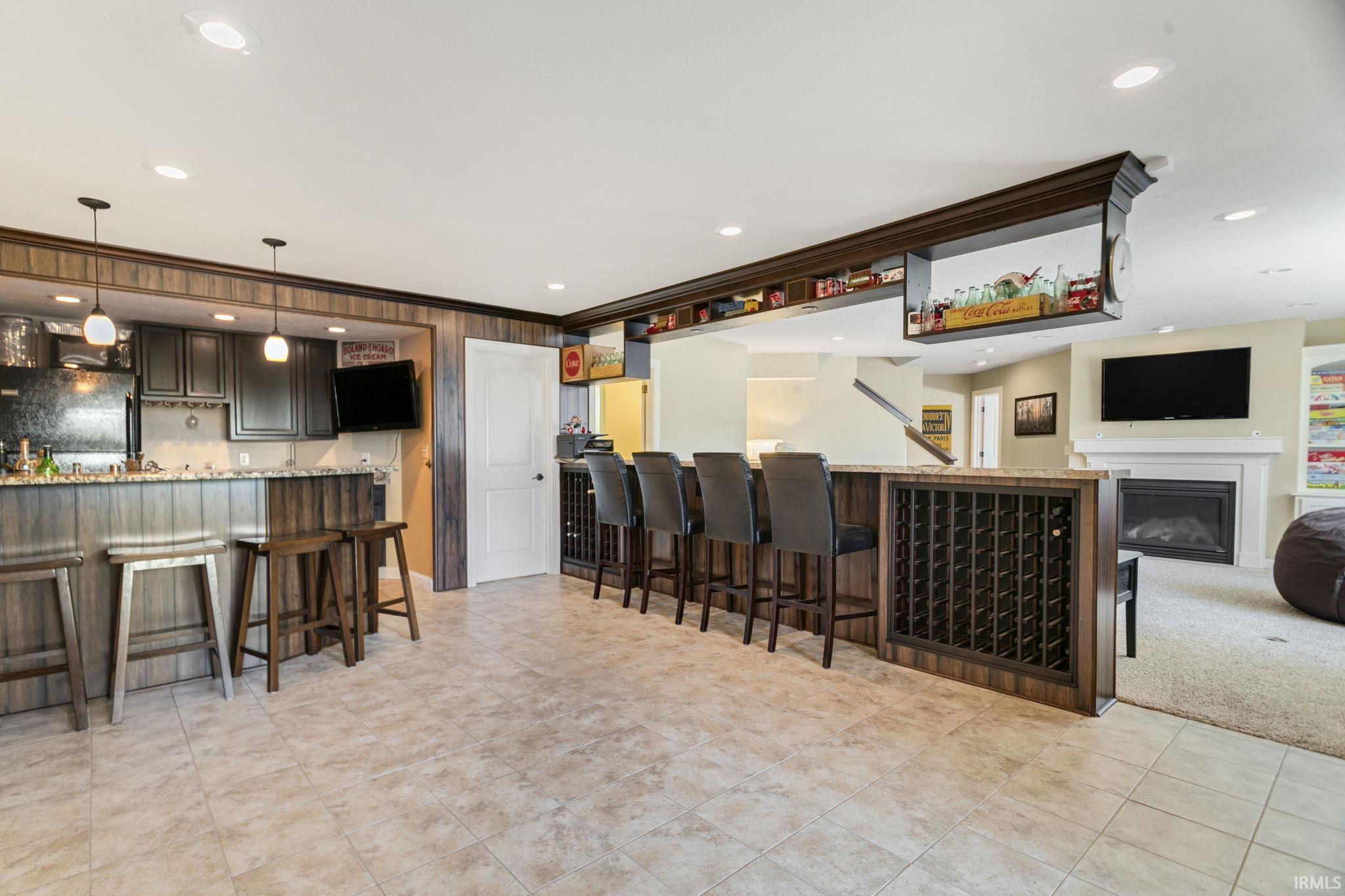 Entertainment area featuring a full bar with built-in wine storage, a fireplace with a mantel, recessed lighting, and tile flooring