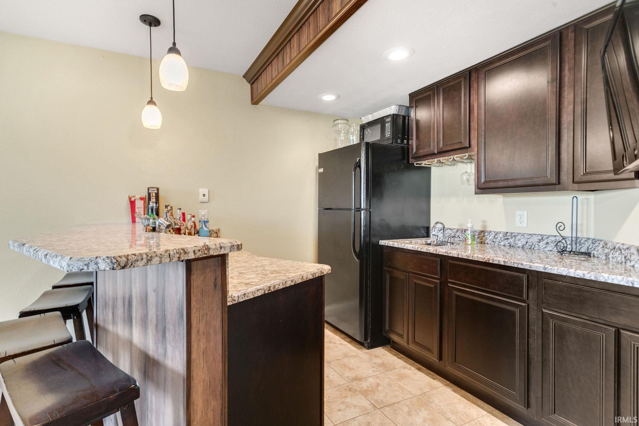 Kitchenette featuring granite countertops, wood-finish cabinetry, a black refrigerator, and tile flooring