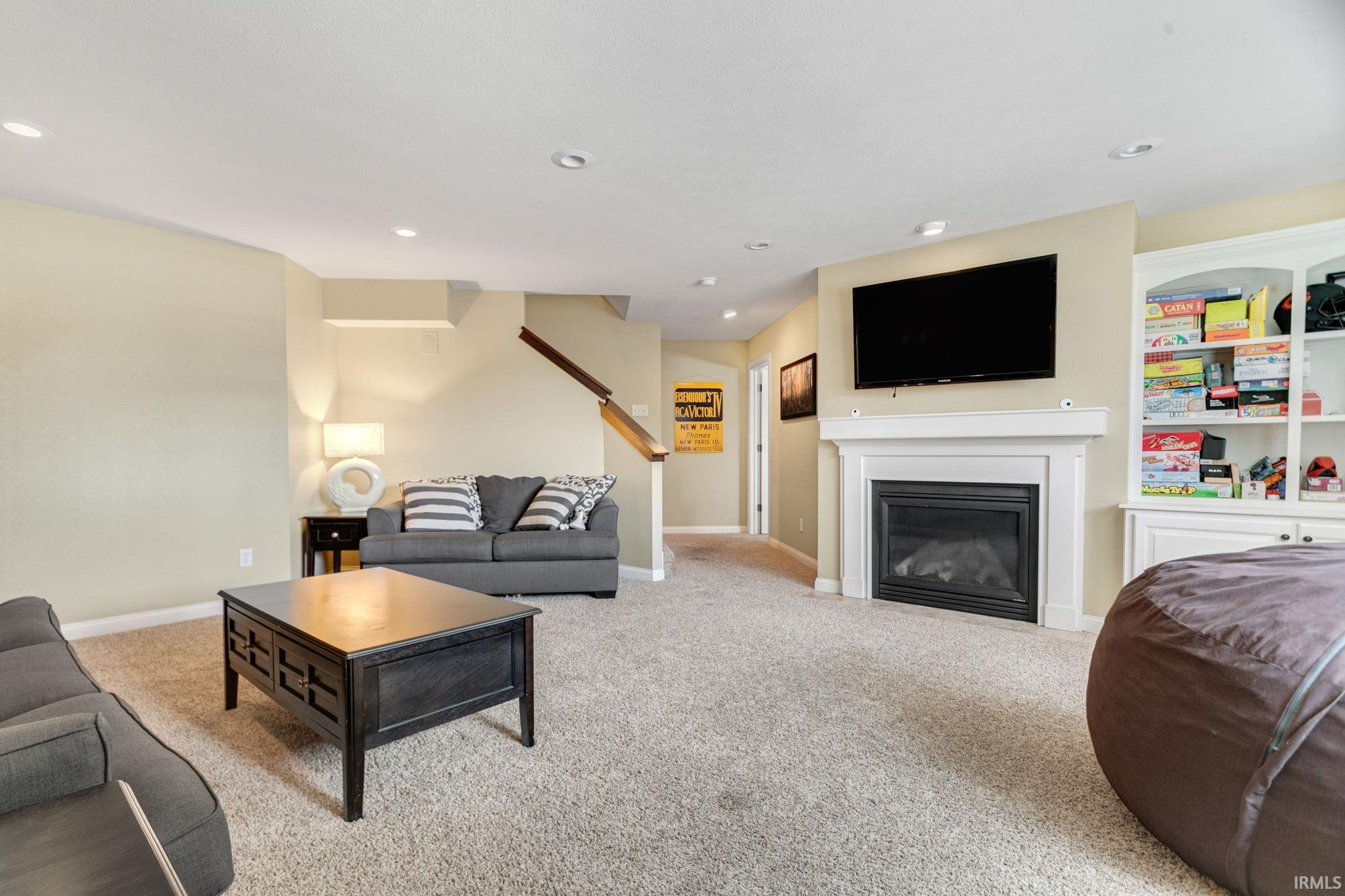Spacious living area featuring neutral carpeting, recessed lighting, a gas fireplace with a white mantel, and built-in white shelving