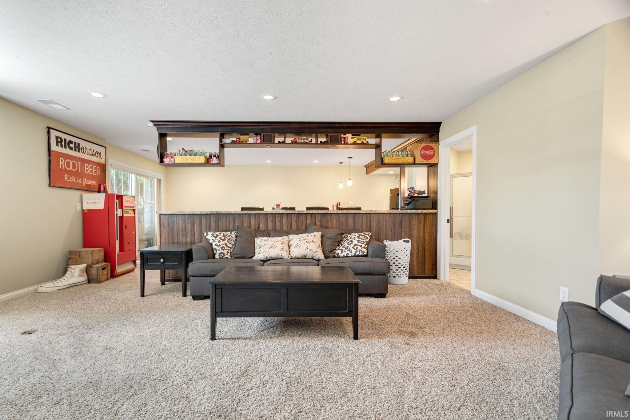 Carpeted recreation room featuring a built-in wet bar with wood-finish paneling, an under-mount sink, and pendant lighting