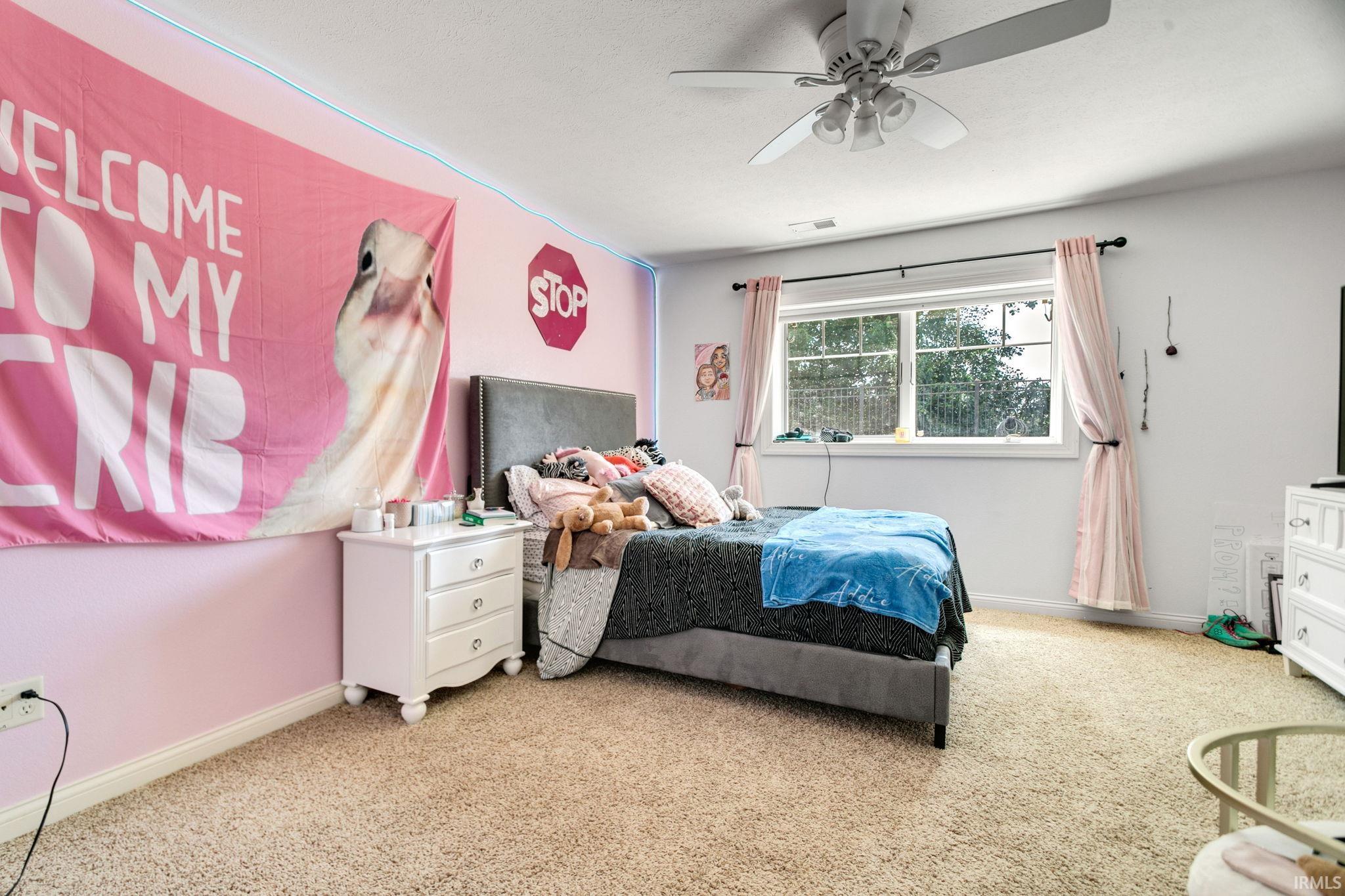 Carpeted room featuring a ceiling fan with light fixture, dual windows with white trim, and a white three-drawer nightstand
