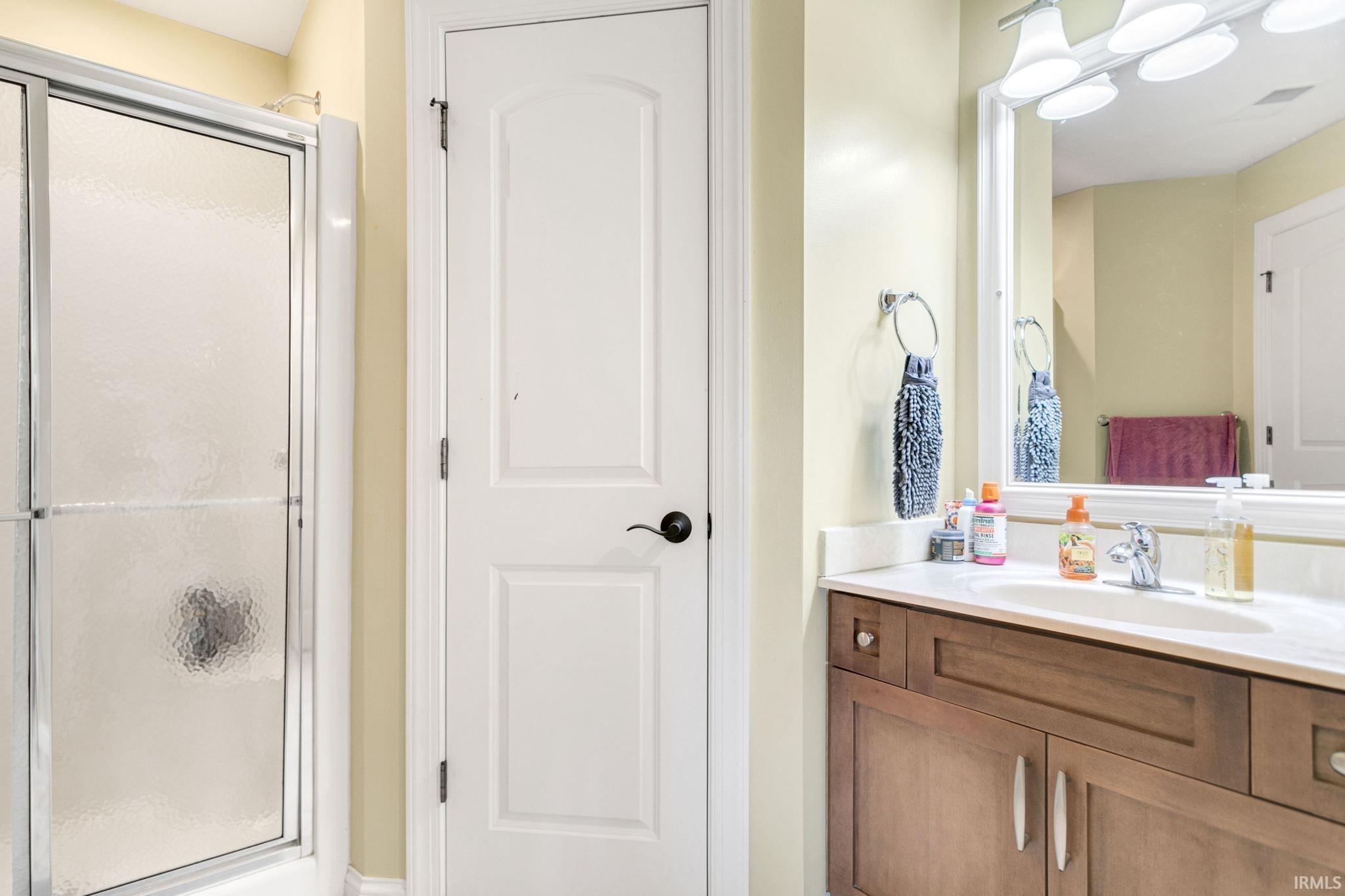 Bathroom featuring a shower with textured glass enclosure, a single vanity with wood-finish cabinetry, a white countertop, and an integrated basin