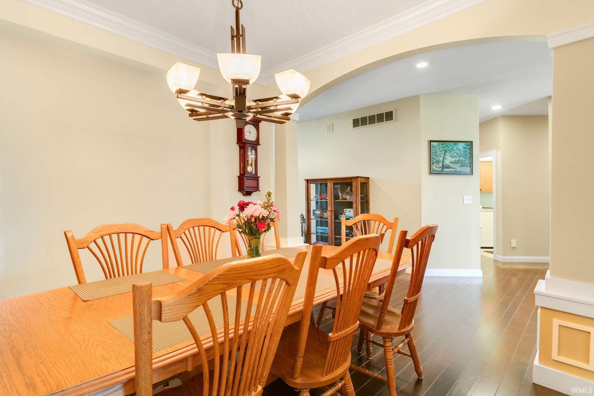 Dining area with dark wood-finish flooring, an arched entryway, recessed lighting, and crown molding