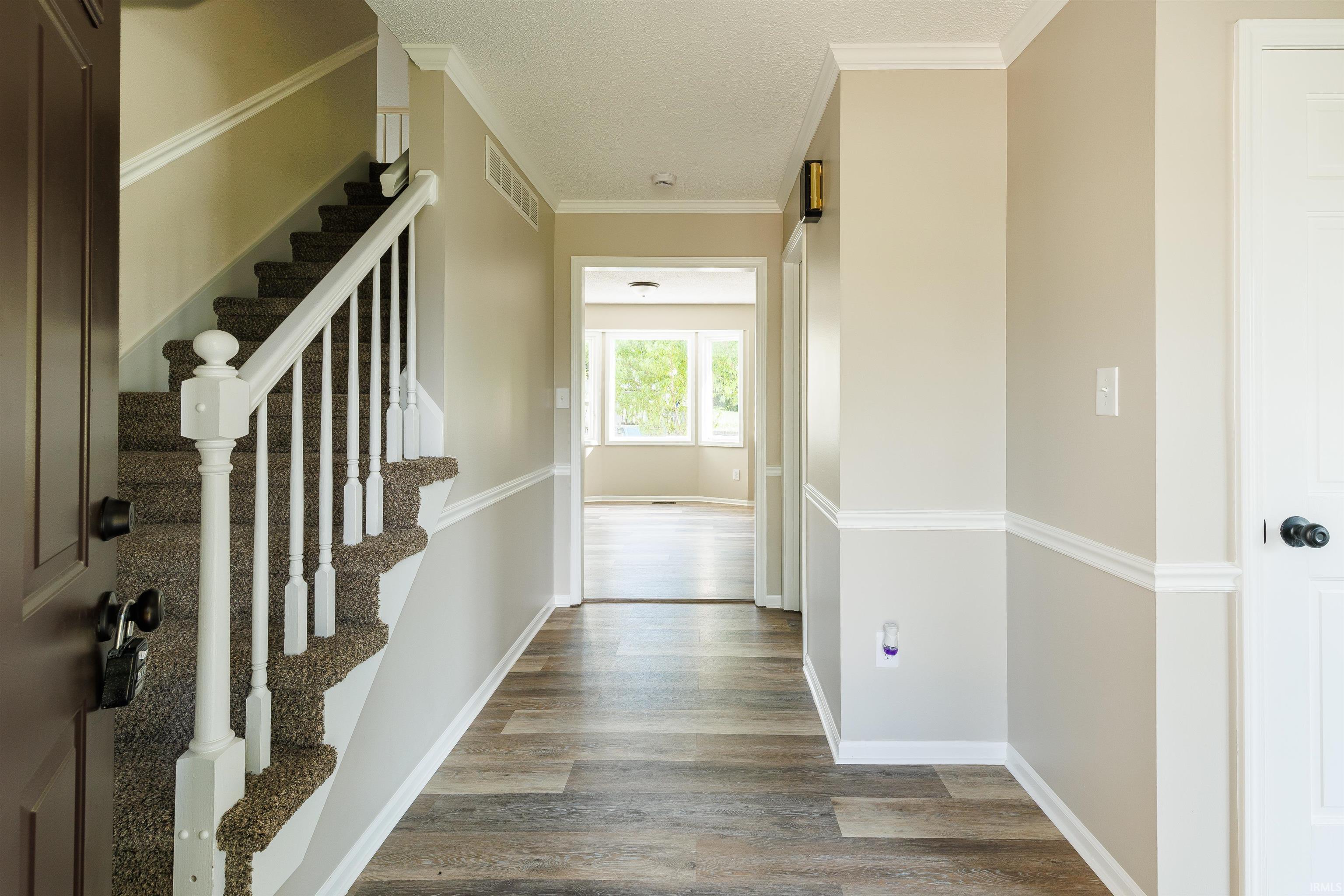 Entryway featuring wood-finish flooring, a carpeted staircase with white balusters, crown molding, chair rail molding, and a paneled interior door
