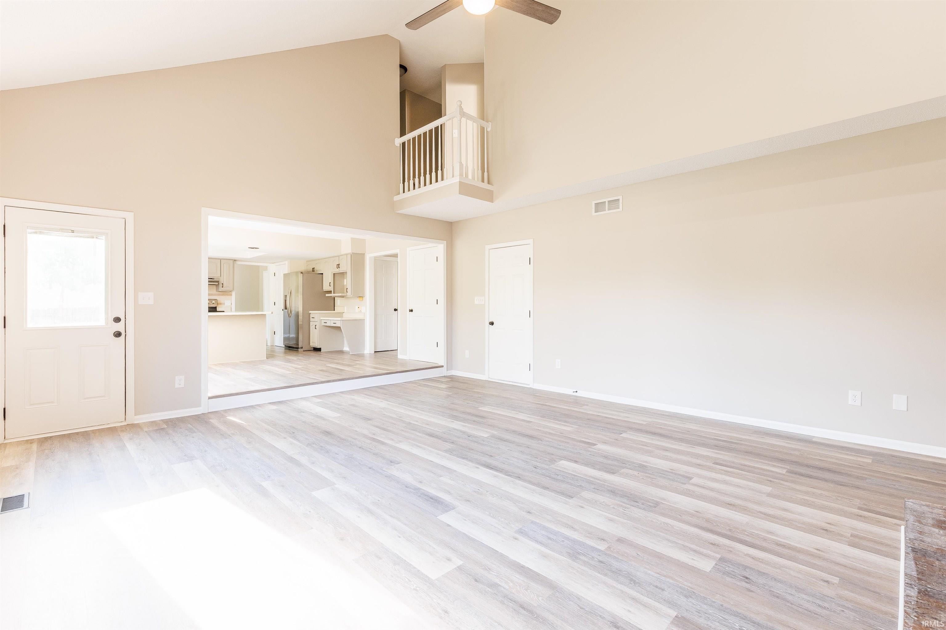 Spacious living area featuring high vaulted ceilings, light wood-finish flooring, a ceiling fan, and a neutral color palette