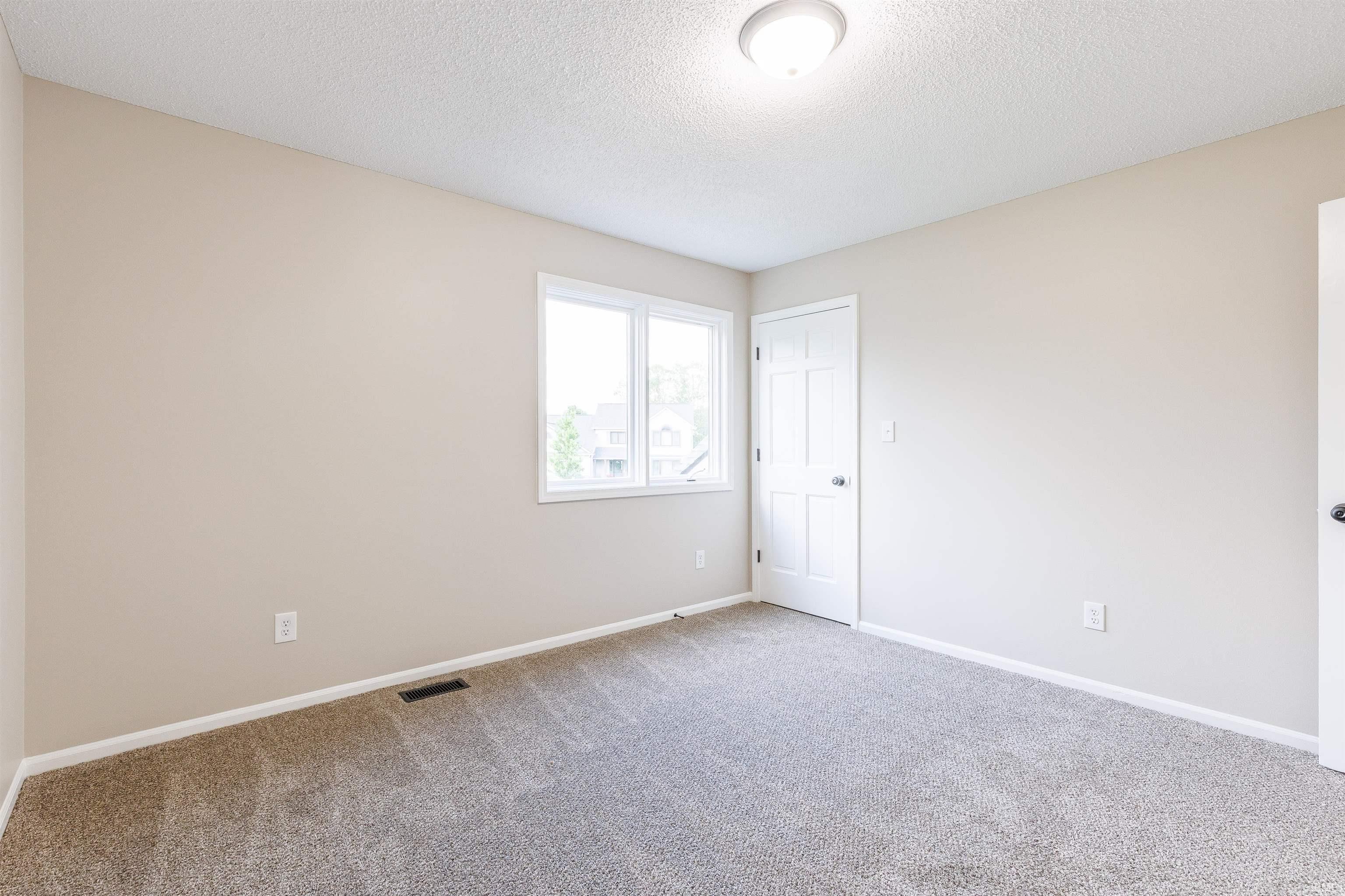 Neutral tone walls featuring a window with exterior views, panel doors, ceiling-mounted light fixture, and textured carpeting