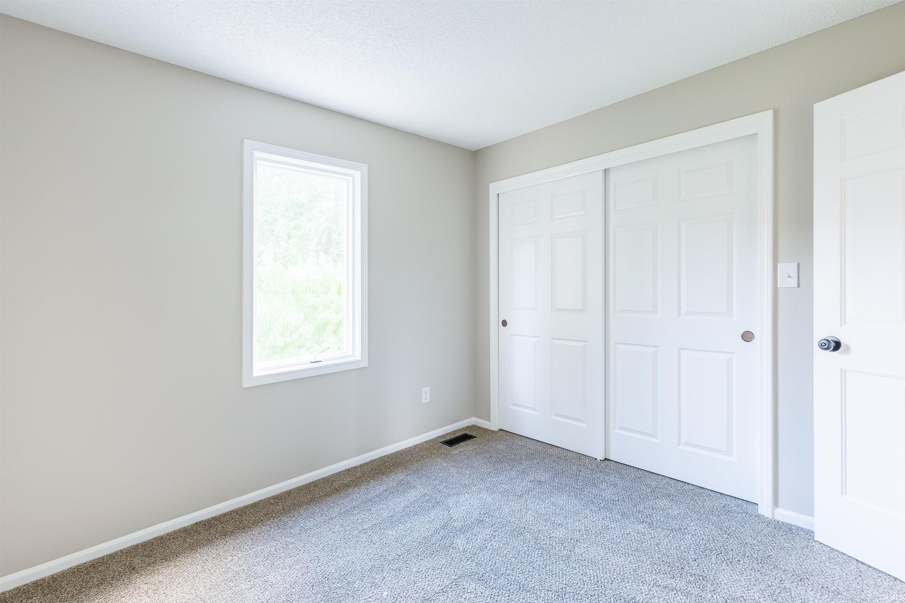 Carpeted room featuring light gray walls, a single window, and a white sliding closet door system