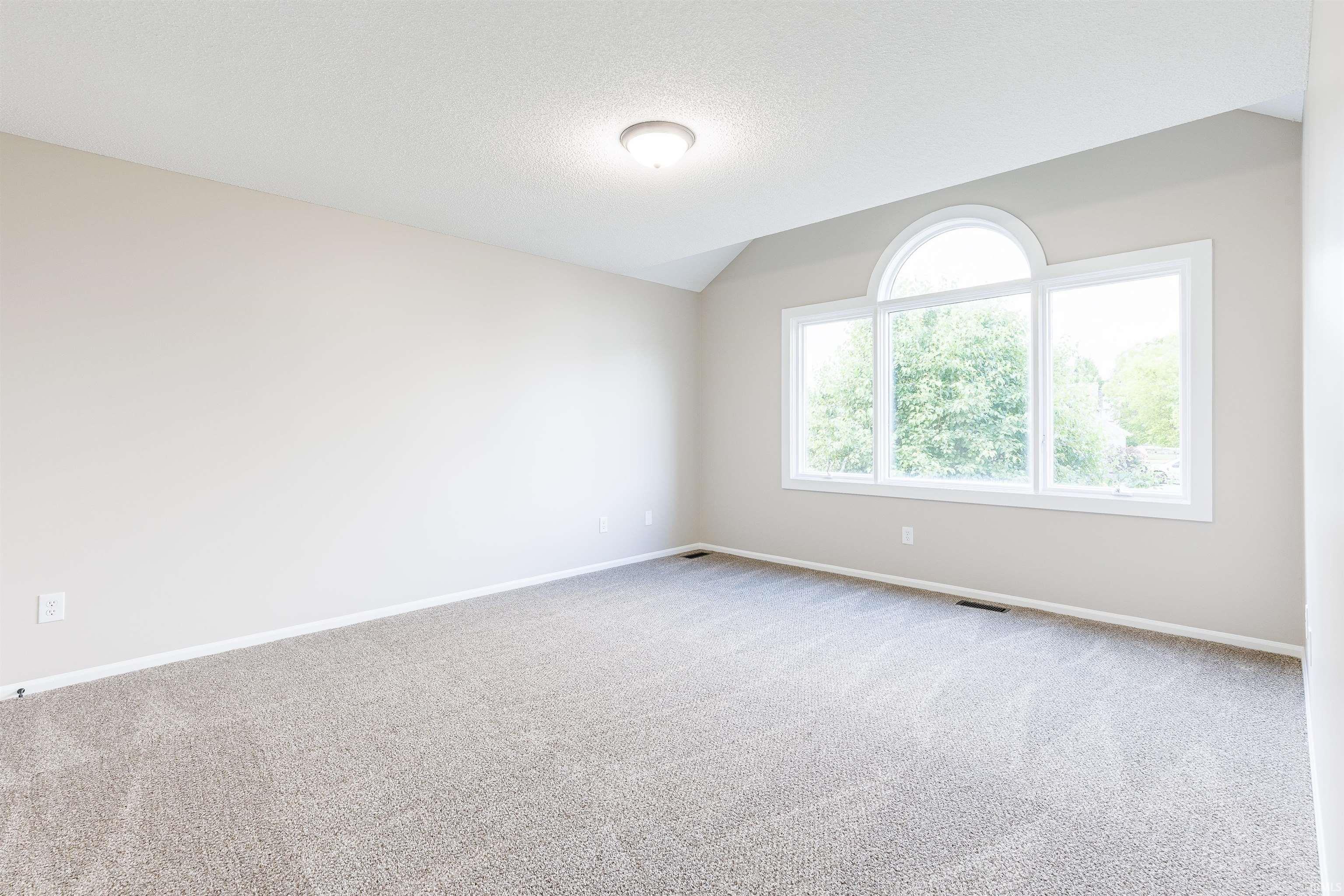 Spacious room featuring vaulted ceilings, a large arched window with two rectangular windows below, neutral carpeting, and light-toned walls