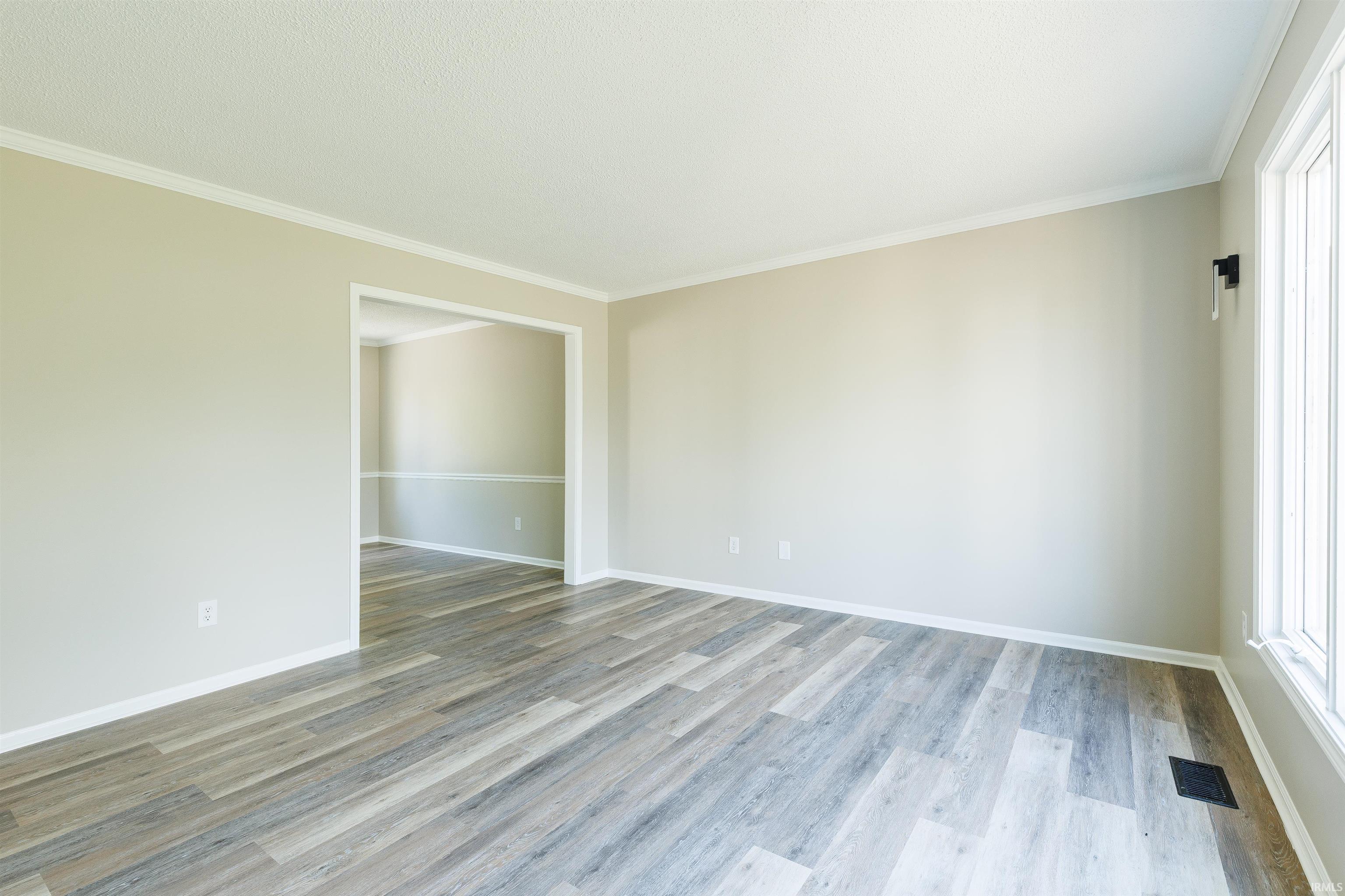 Spacious interior room featuring wood-finish flooring, neutral wall tones, white crown molding, white baseboards, and a large window with white trim