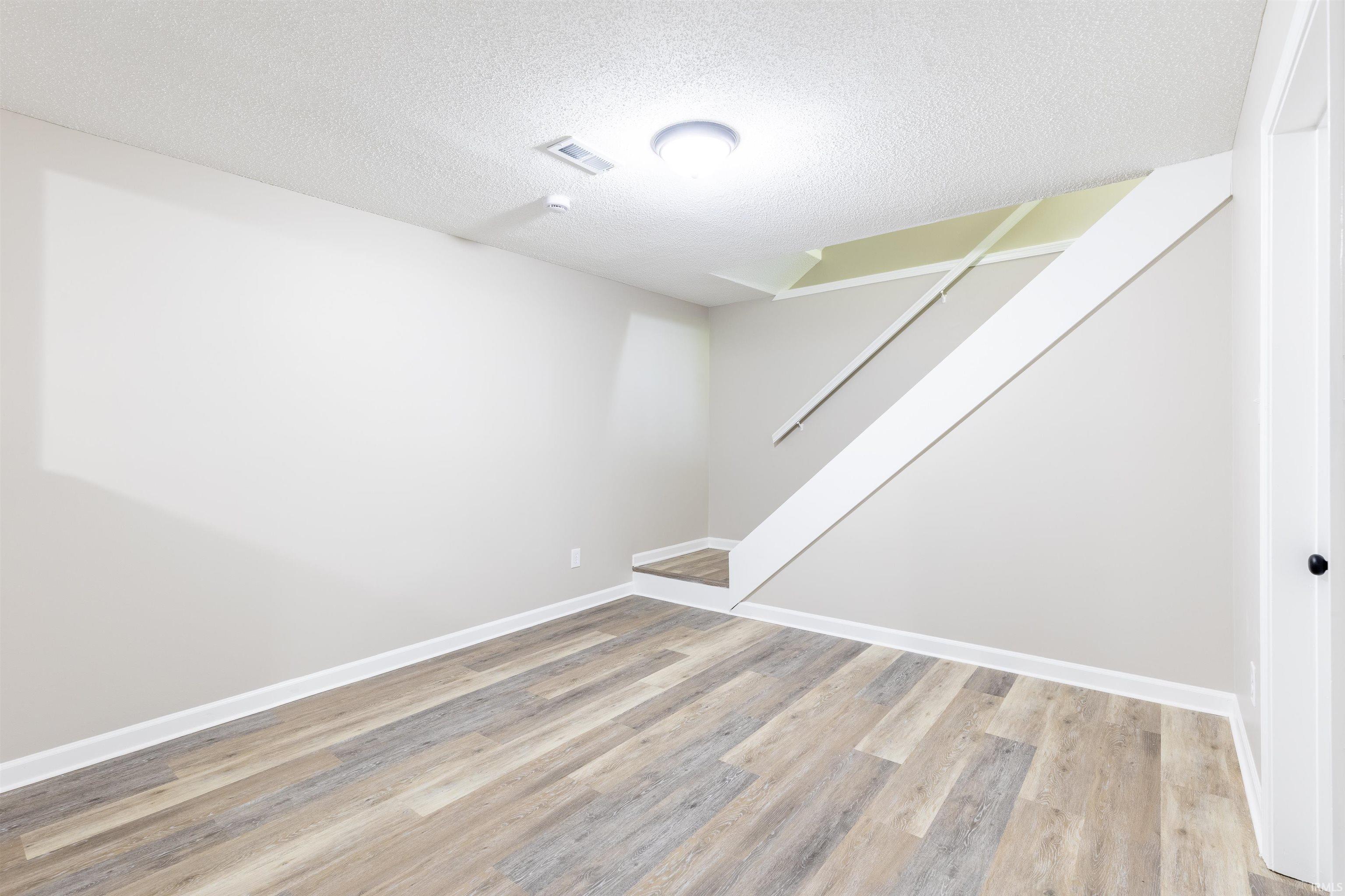 Spacious room featuring wood-finish flooring, light neutral walls, white trim, and a contemporary ceiling light fixture
