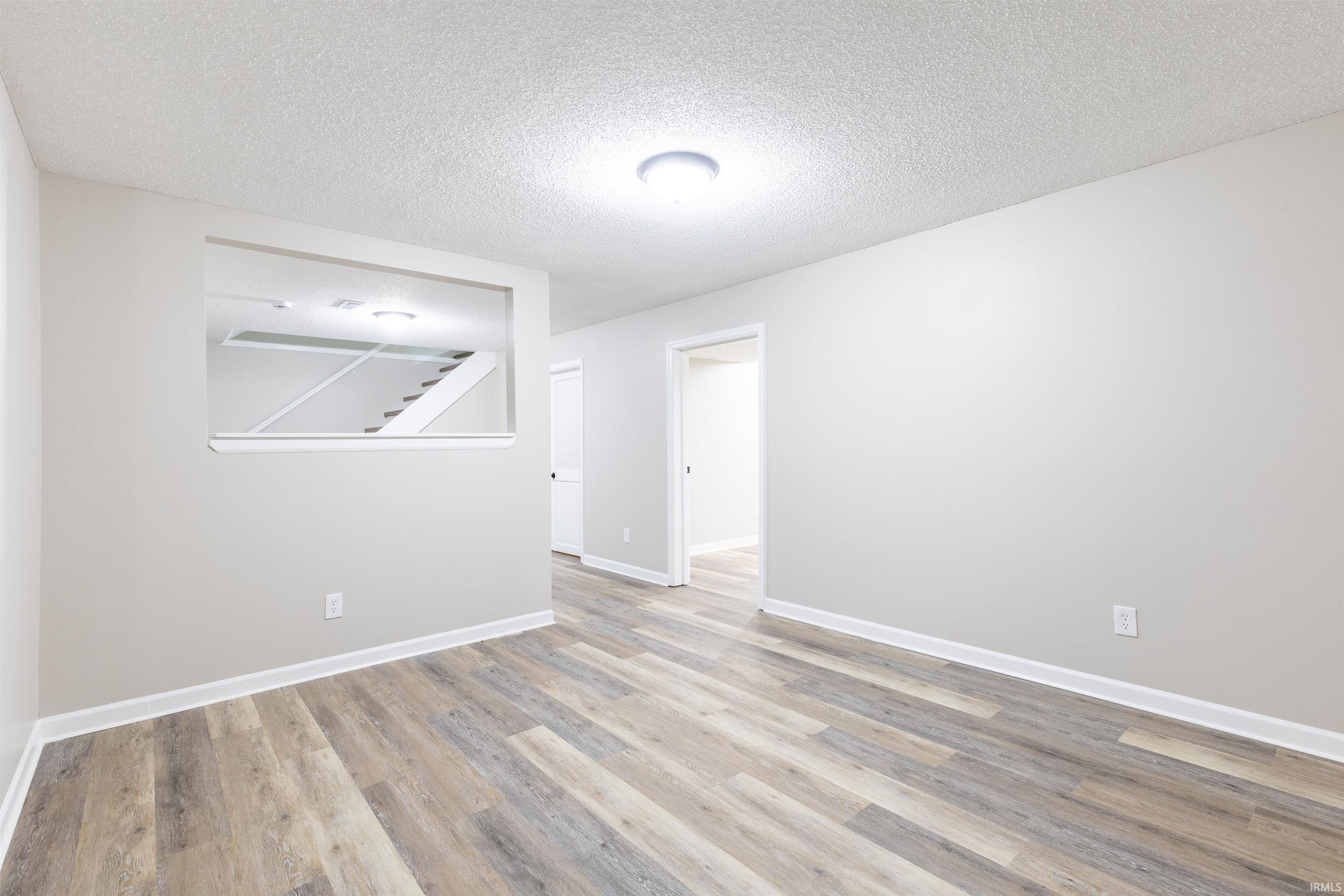 Spacious room featuring wood-finish flooring, light grey painted walls, white baseboards, and a ceiling-mounted light fixture