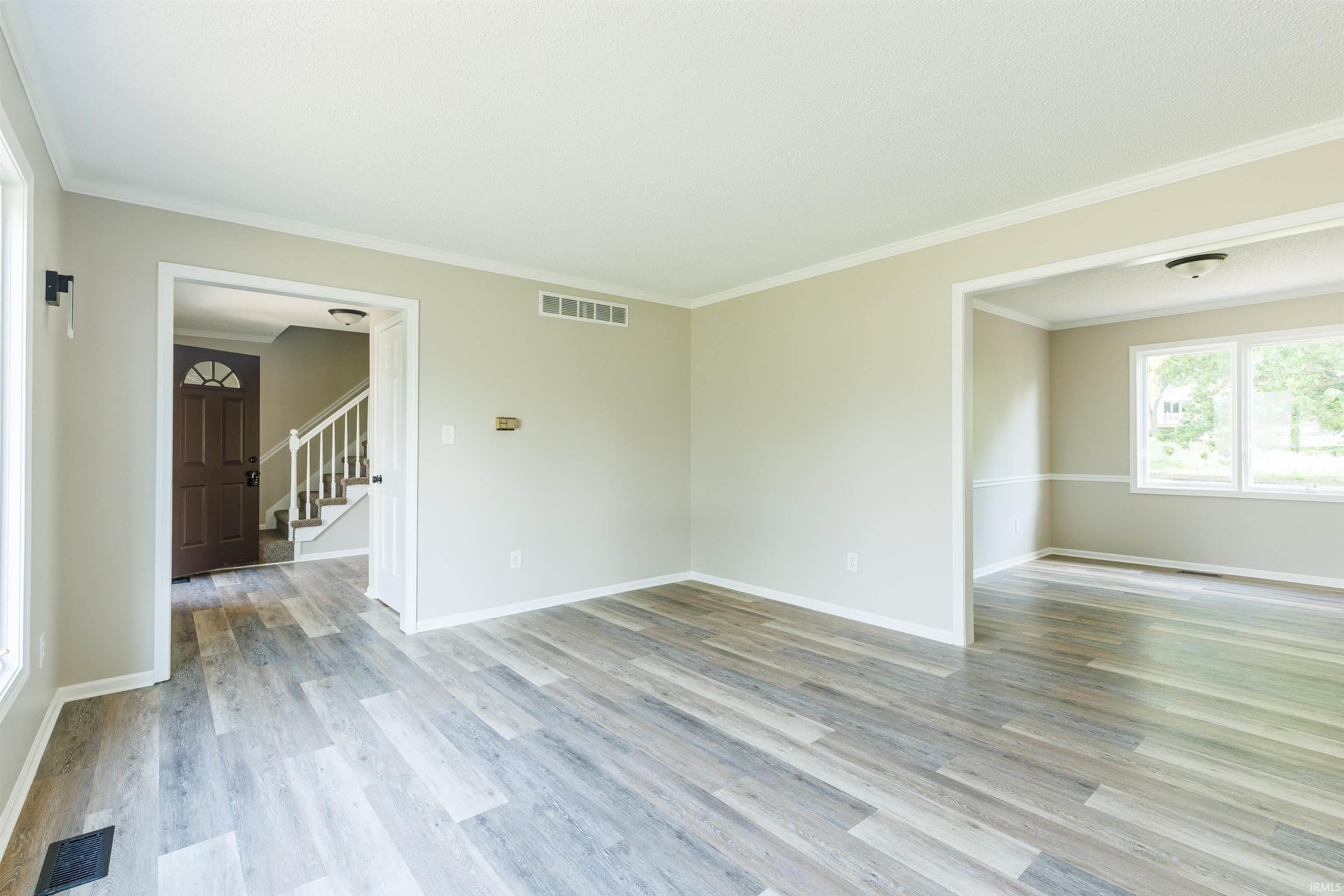 Spacious interior featuring wood-finish flooring, neutral wall tones, white trim, and an open doorway to an additional room