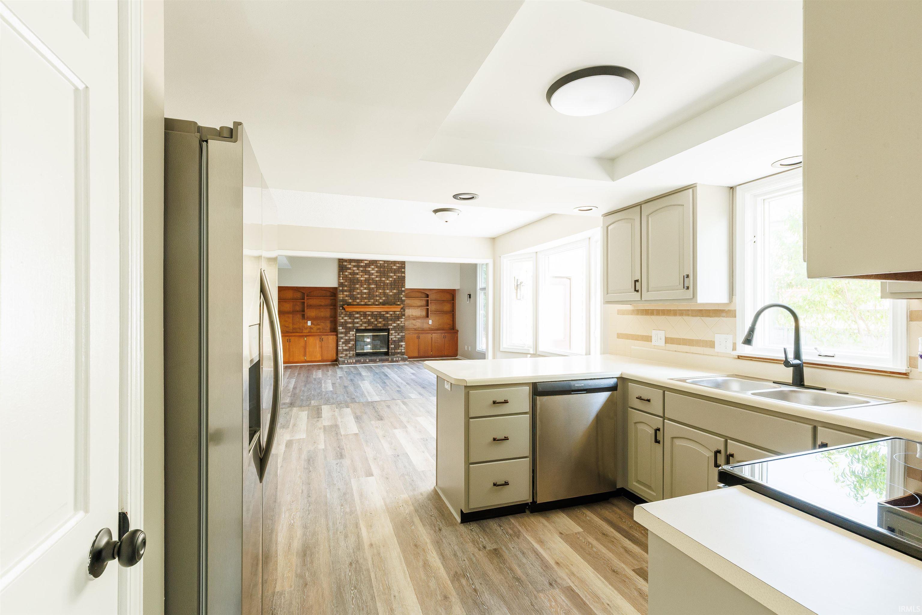 Open-concept kitchen featuring wood-finish flooring, light-toned cabinetry, stainless steel appliances, a center island, and a black gooseneck faucet