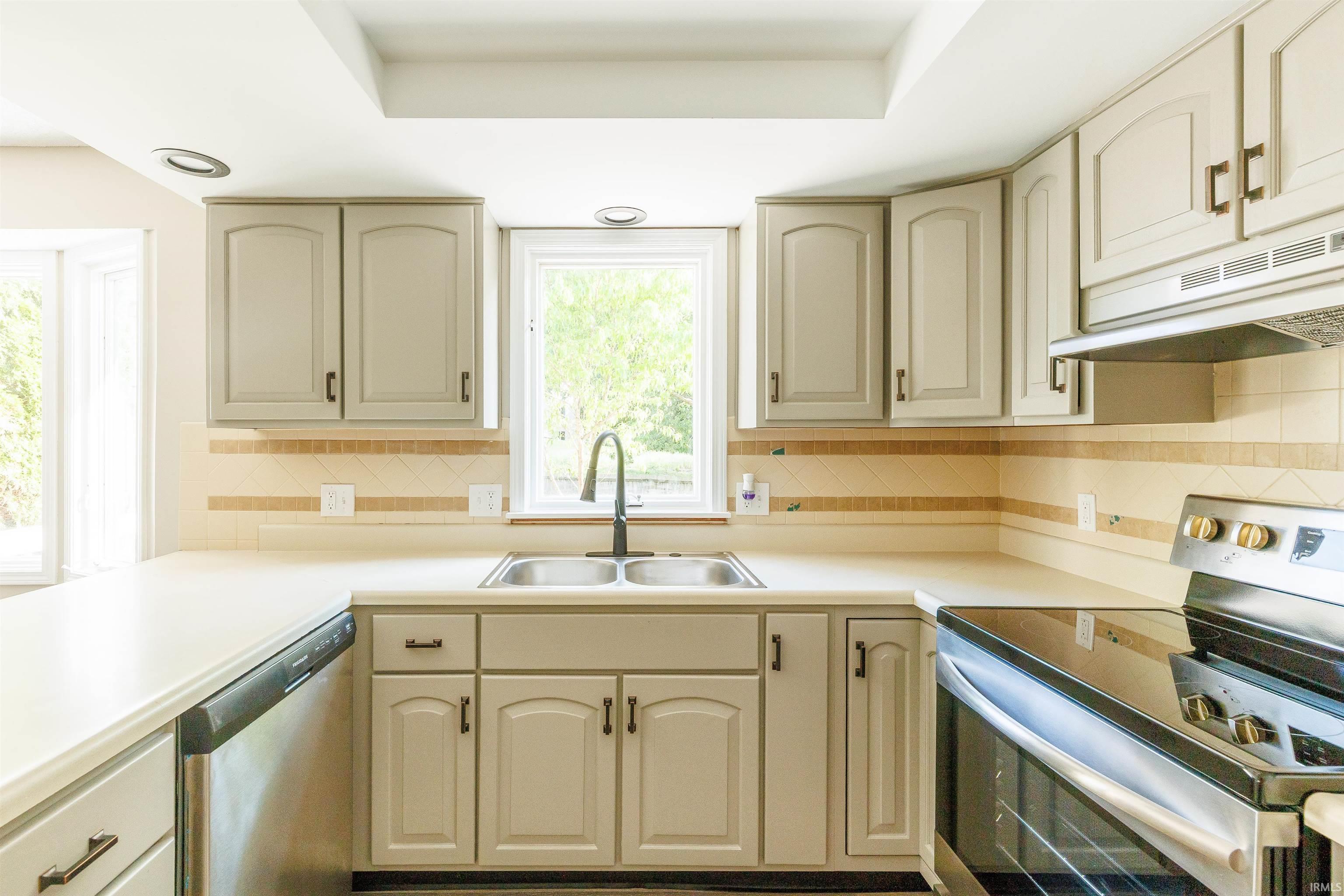Kitchen featuring light-toned cabinetry with dark hardware, a double basin stainless steel sink with a dark gooseneck faucet, light countertops, and a tiled backsplash