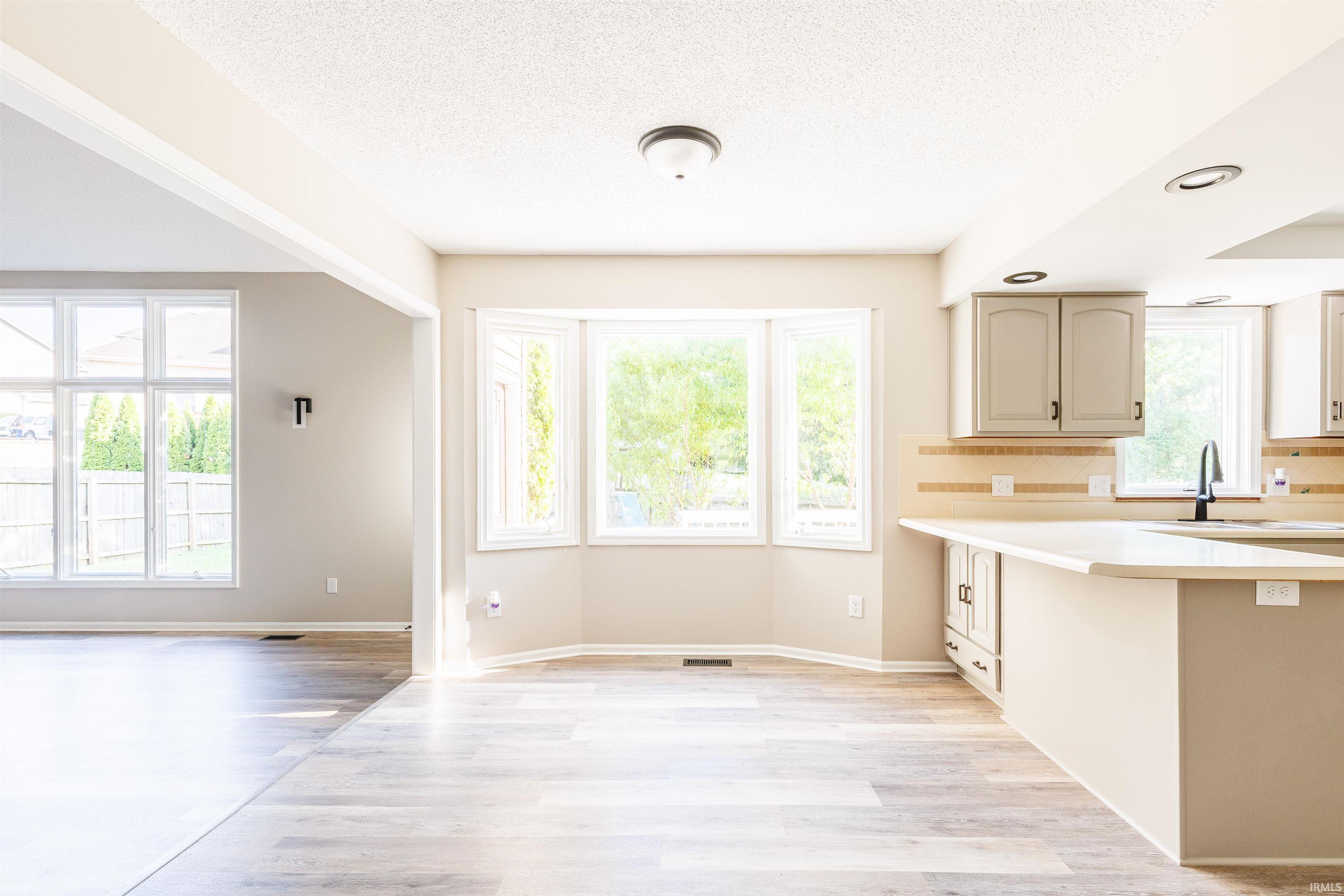 Bright interior space featuring wood-finish flooring, a kitchen island with light-toned countertops, grey cabinetry with dark hardware, a bay window, and recessed lighting