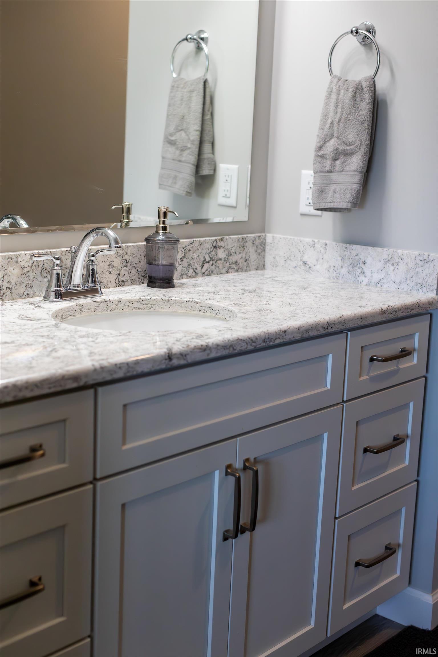 Bathroom vanity featuring a light-toned countertop with integrated sink, chrome faucet, and expansive mirror