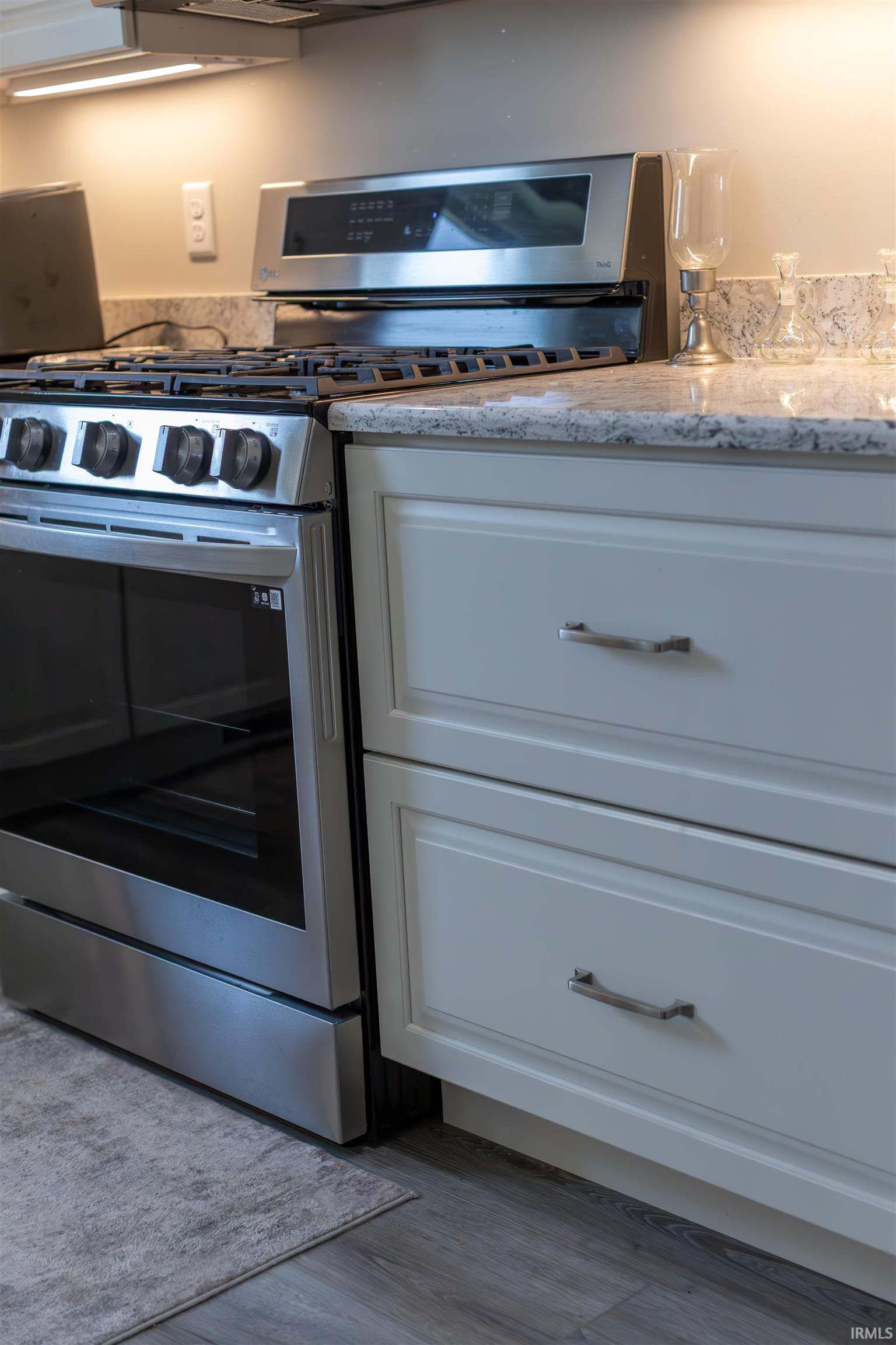 Stainless steel range with gas cooktop, light-toned cabinetry, light-colored countertops, and wood-finish flooring
