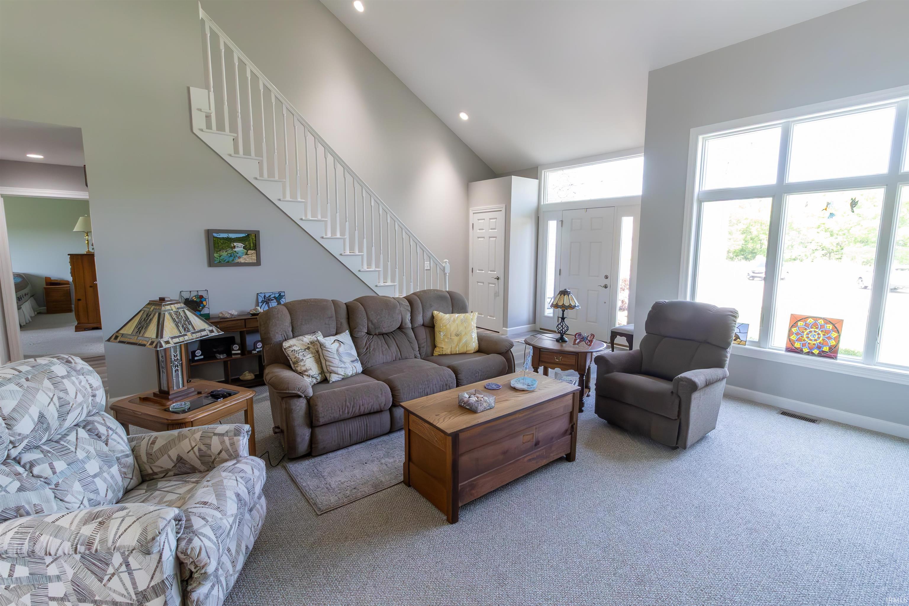 Living area featuring a prominent staircase with white railings, a front entry door with transom window, and large windows