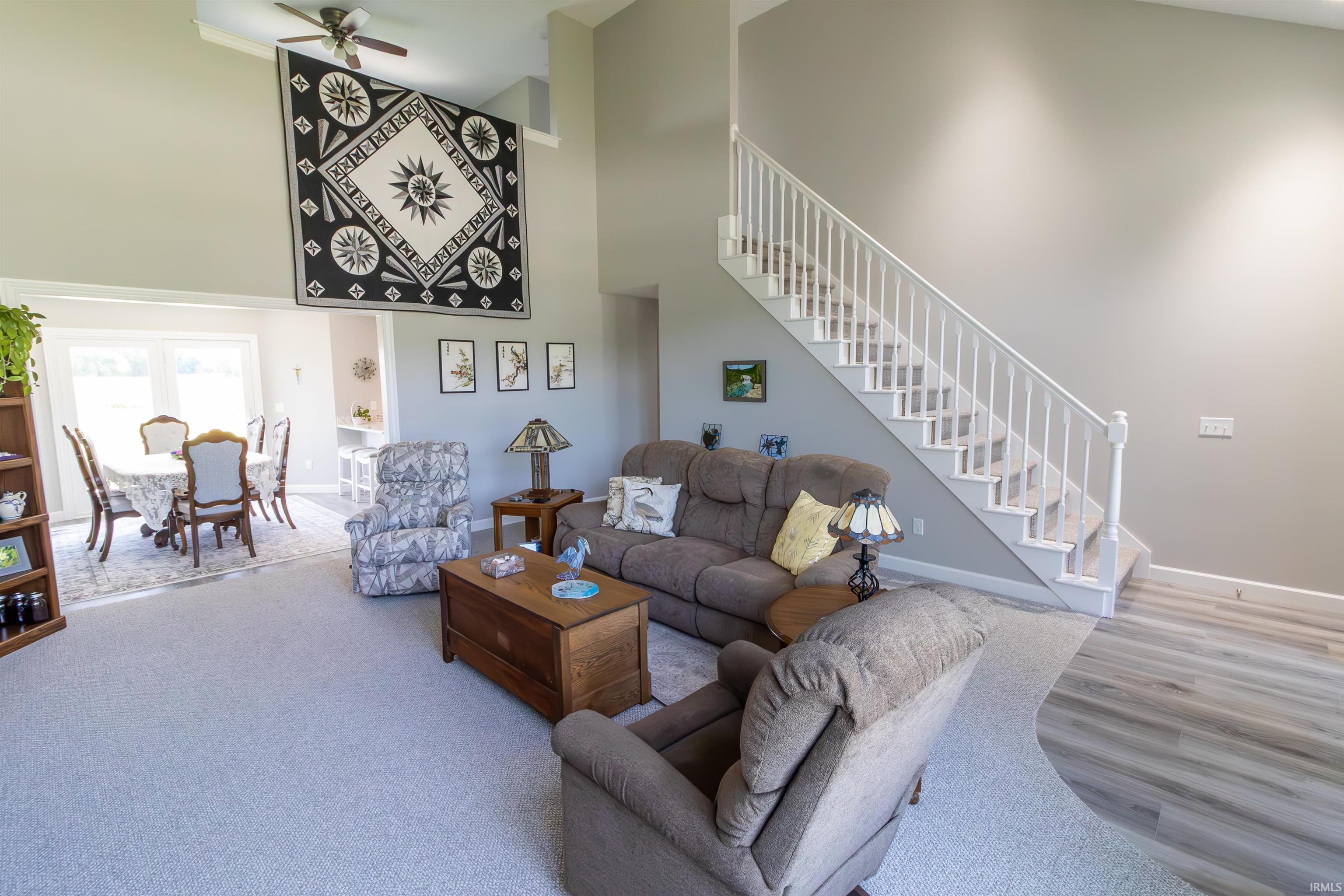 Spacious living area featuring a high vaulted ceiling, ceiling fan, and carpeted flooring