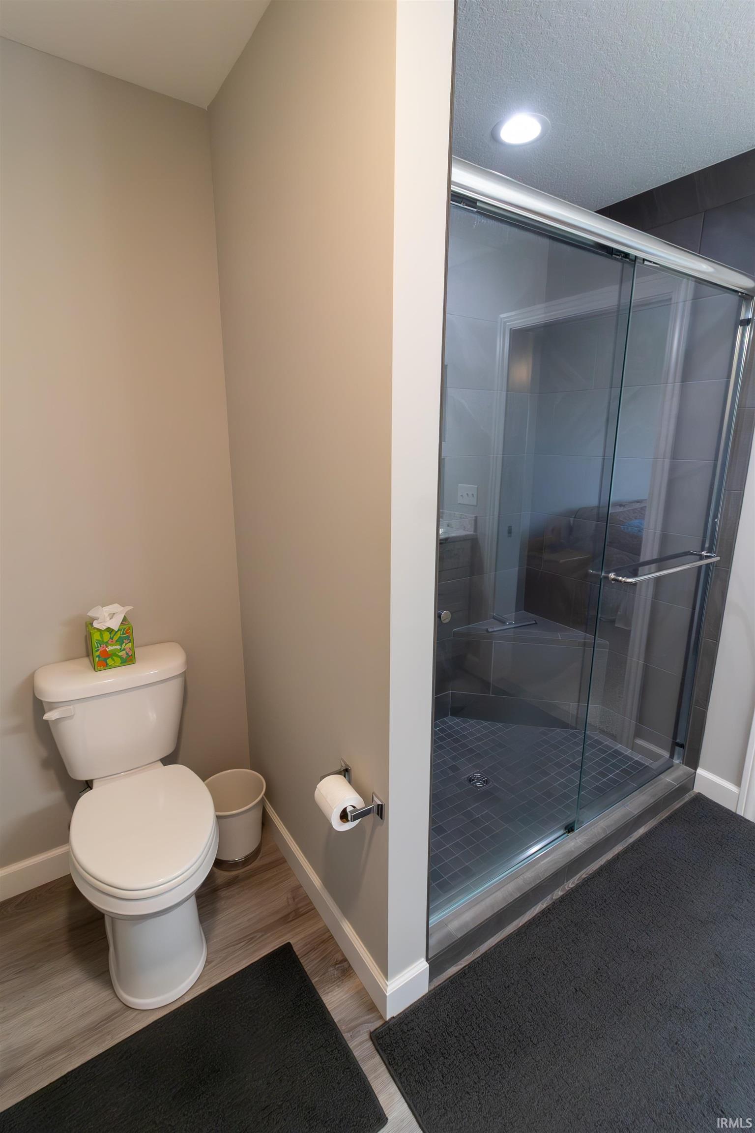 Glass-enclosed shower with dark tile surround and recessed lighting