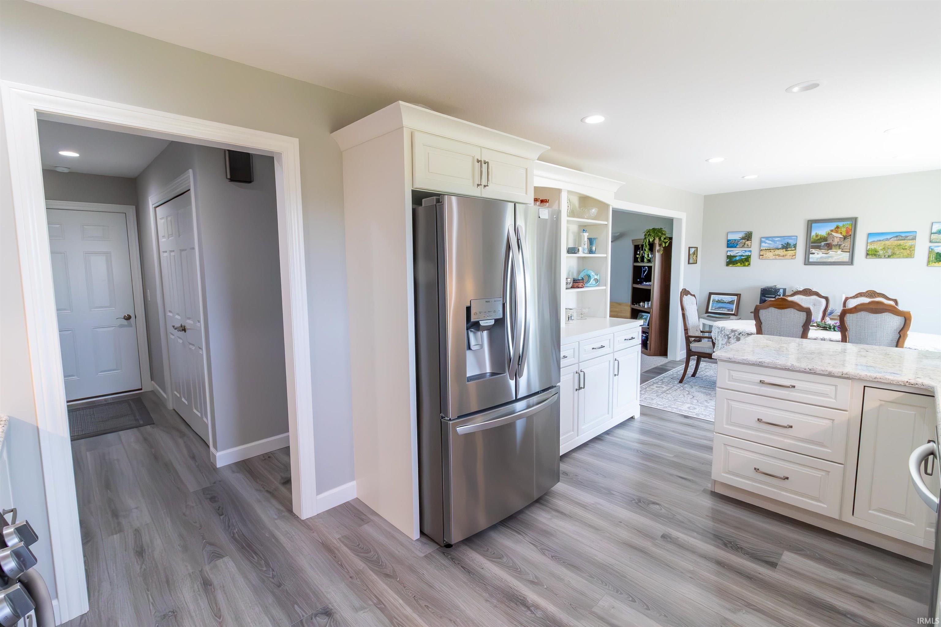 Kitchen area featuring wood-finish flooring, white cabinetry, a built-in stainless steel refrigerator, and recessed lighting