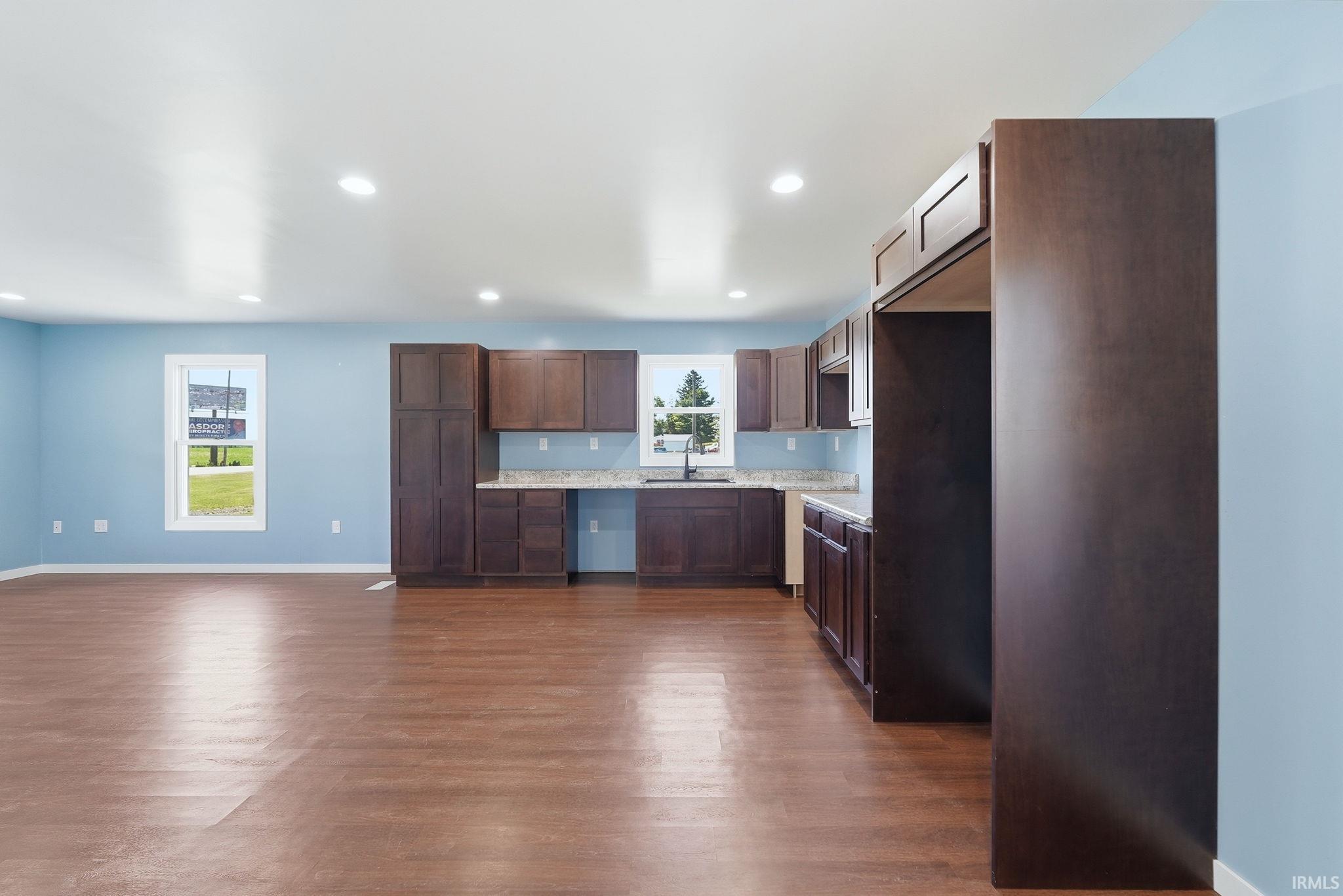 Open-concept living area with wood-finish flooring, recessed lighting, and a kitchen featuring dark wood cabinetry, light-toned countertops, and a stainless steel sink with a gooseneck faucet