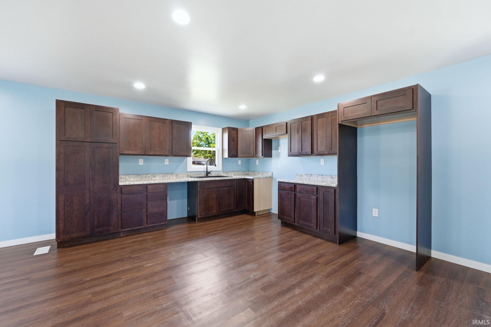 Kitchen featuring abundant dark wood-finish cabinetry, granite-style countertops, and wood-finish flooring