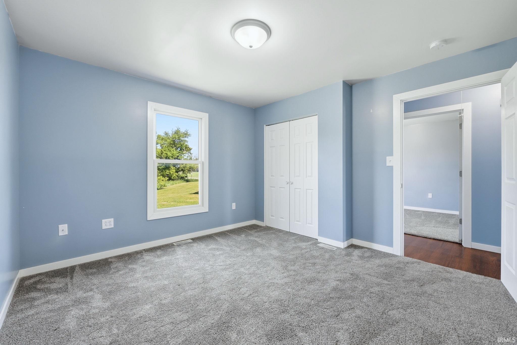 Room featuring light blue walls, gray carpet, a double-panel closet door, and a window with white trim