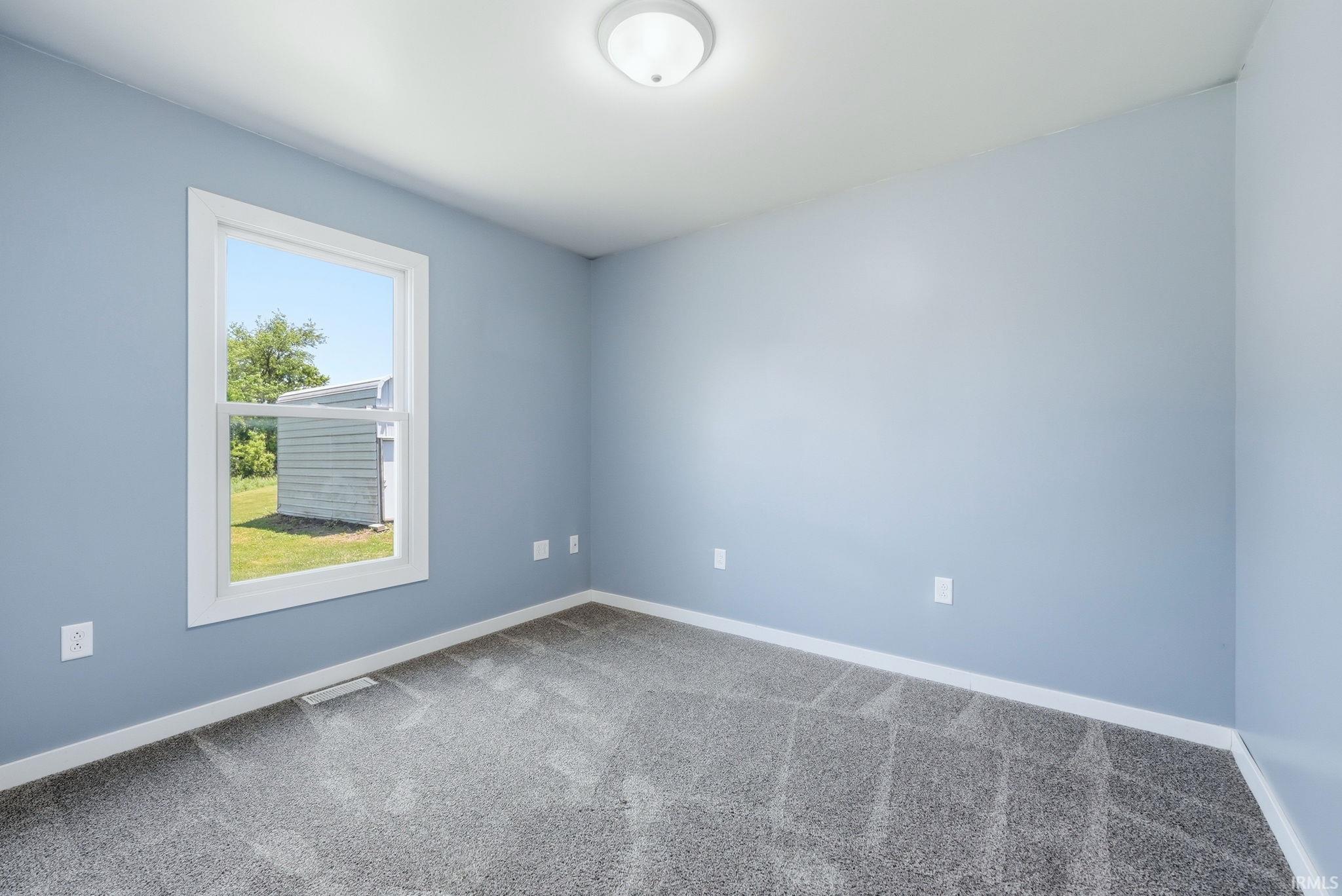 Bright interior featuring a single window, light blue walls, gray patterned carpeting, white trim, and a flush-mount ceiling light fixture