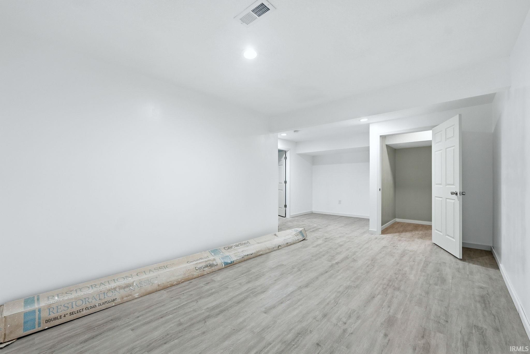 Spacious interior room featuring light wood-finish flooring, recessed lighting, white walls, and a closet with a white paneled door
