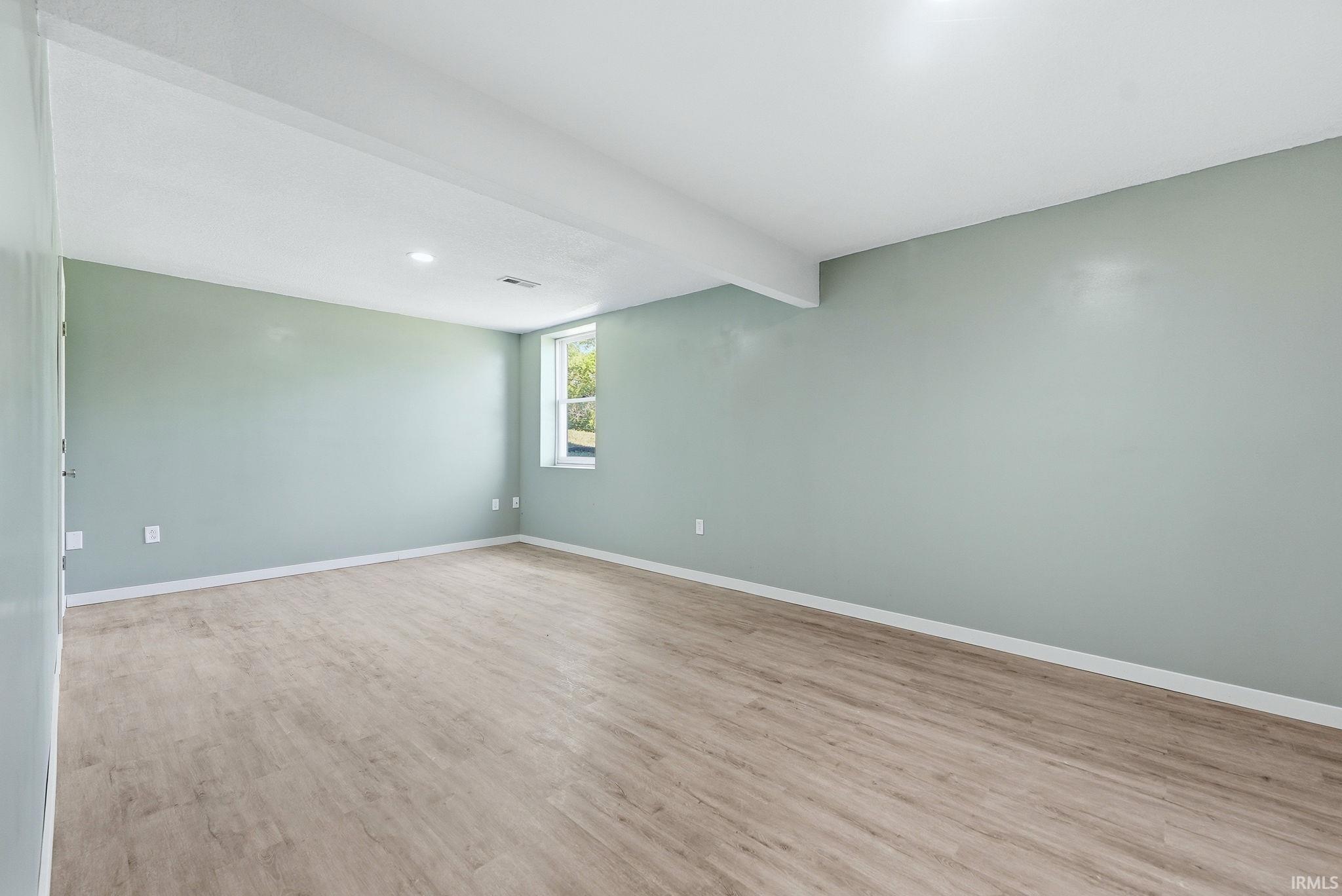 Spacious room featuring wood-finish flooring, light green walls, a window offering natural light, and recessed lighting