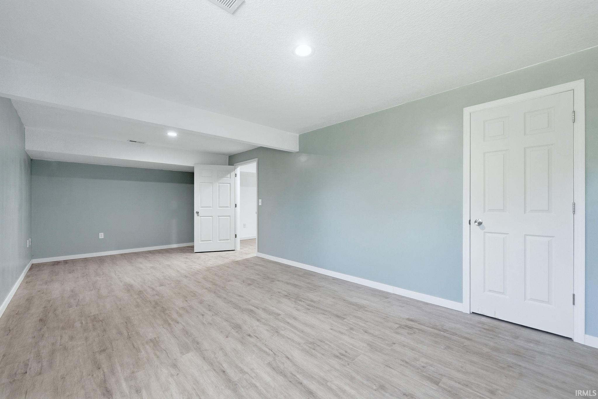 Spacious interior room featuring wood-finish flooring, light blue walls, white baseboards, and recessed lighting