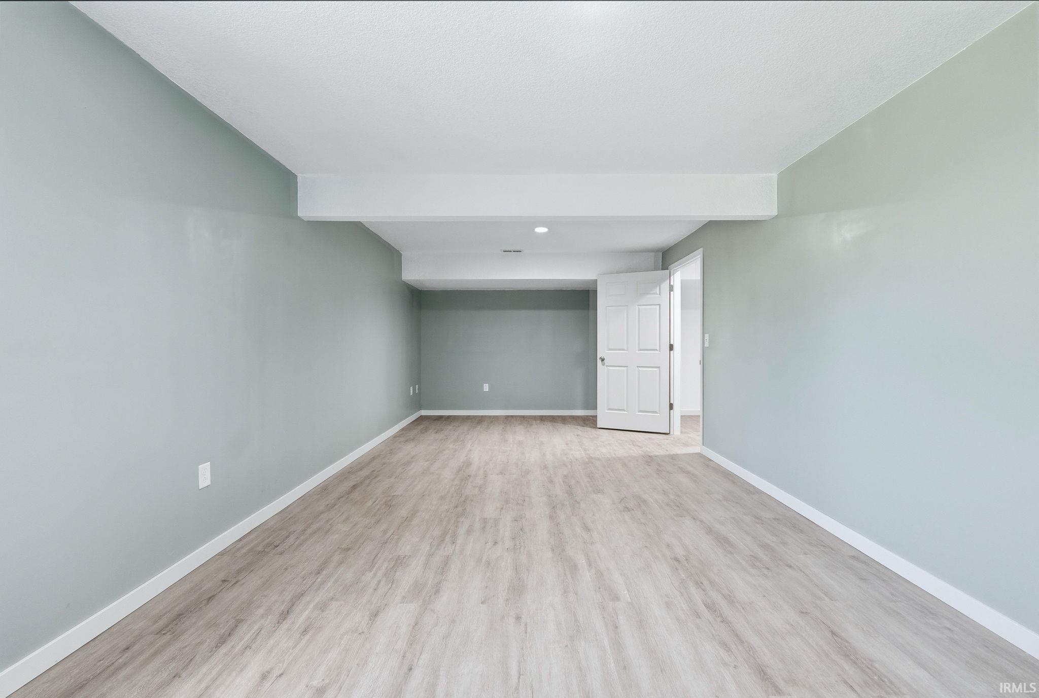 Spacious room featuring light wood-finish flooring, light blue-green wall paint, white trim, and recessed lighting