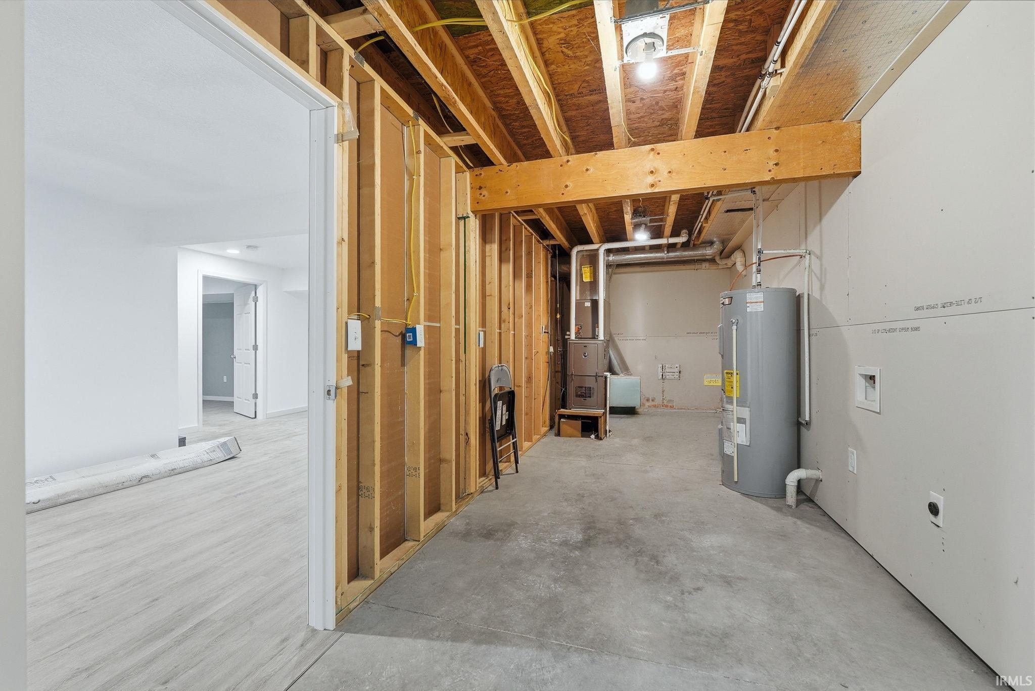 Unfinished basement space featuring exposed wood framing, concrete flooring, and a water heater
