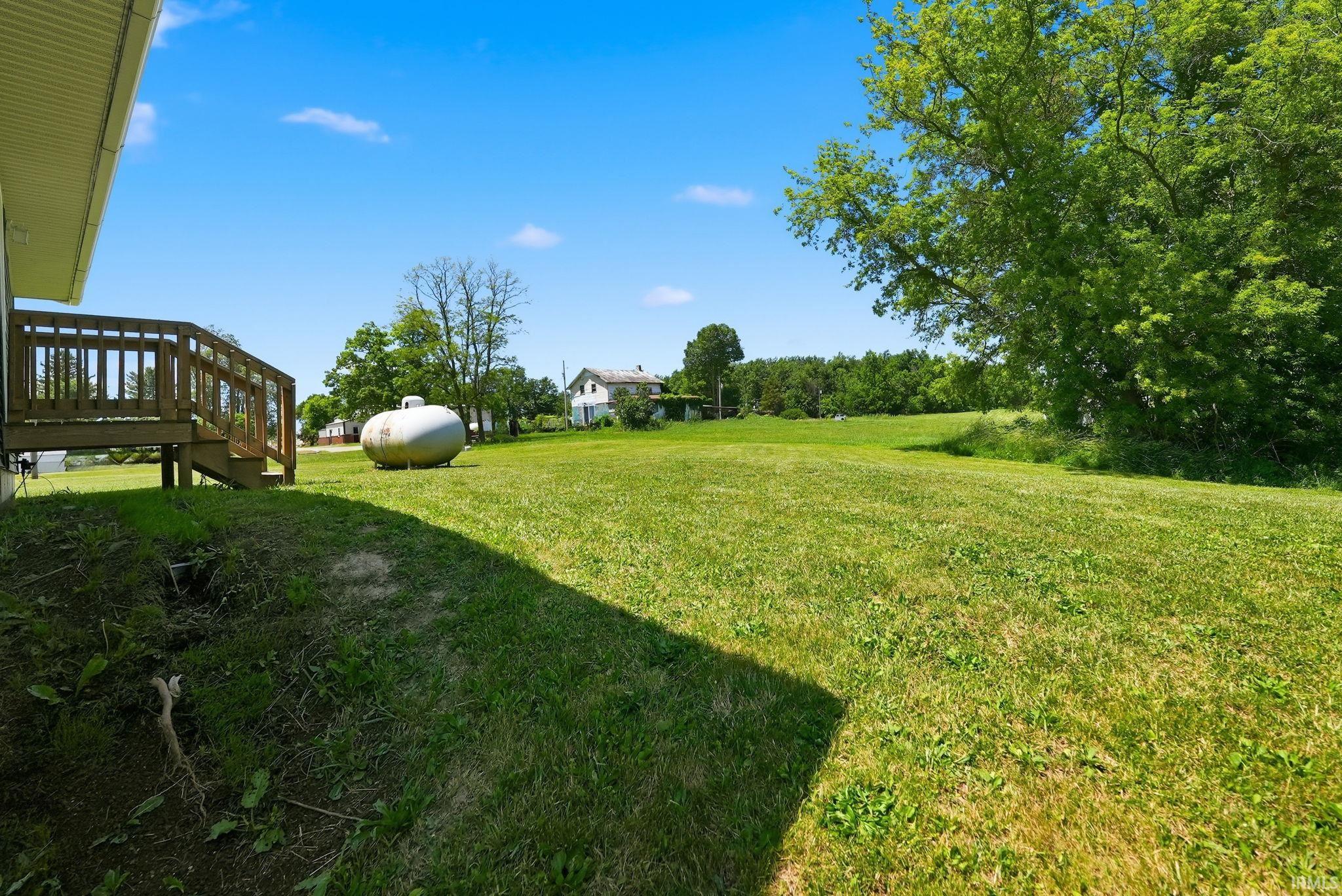 Expansive green lawn extending to the horizon, featuring mature trees and a wooden deck with railing