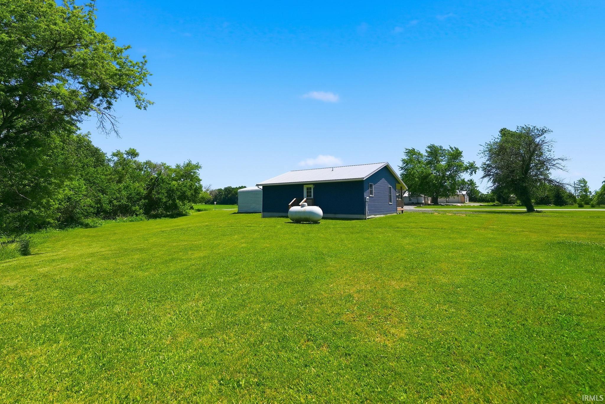 Expansive green lawn with mature trees and a detached structure featuring blue siding and a metal roof